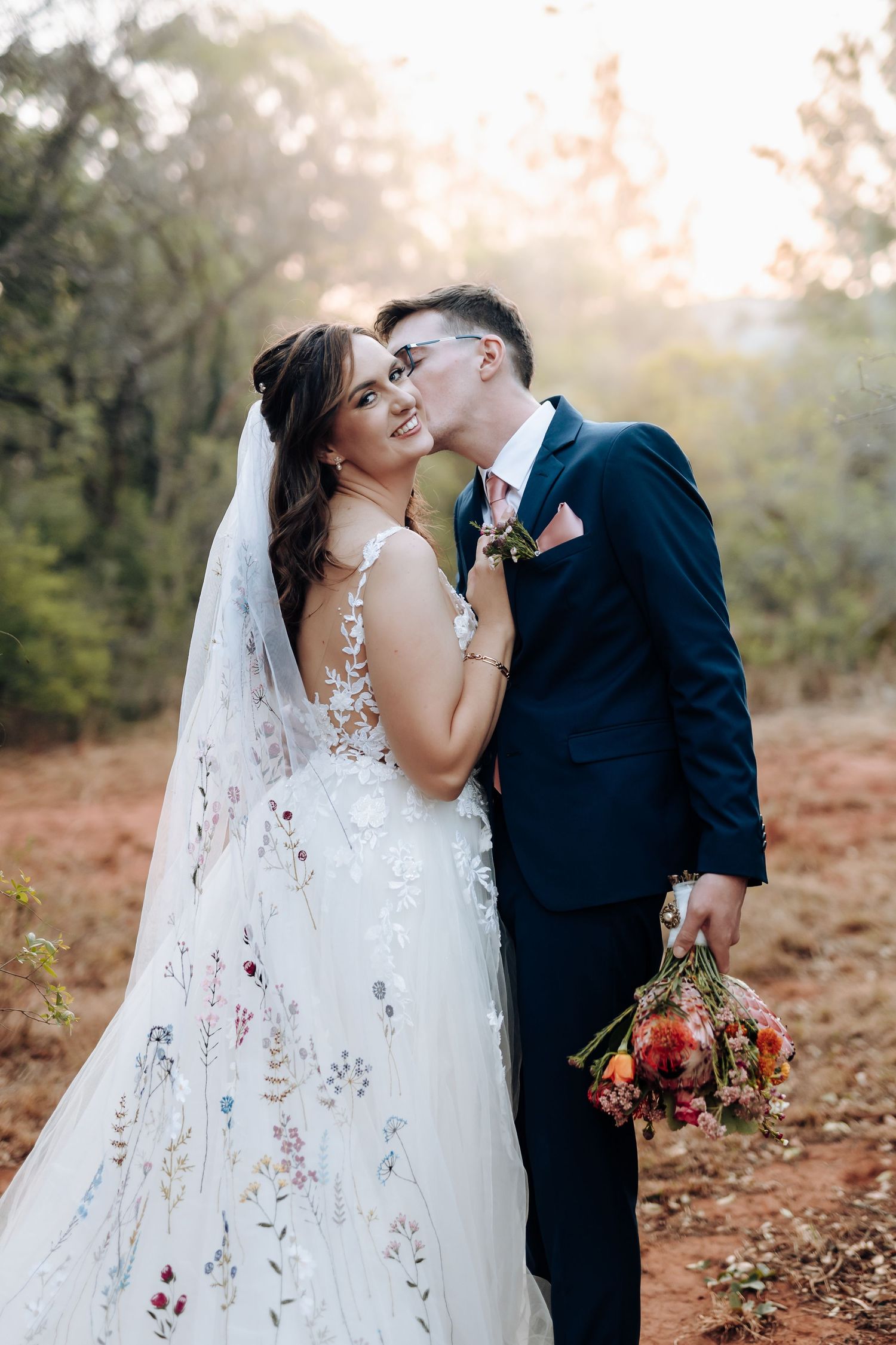 A couple in wedding attire shares intimate moments during an outdoor autumn photoshoot at sunset.