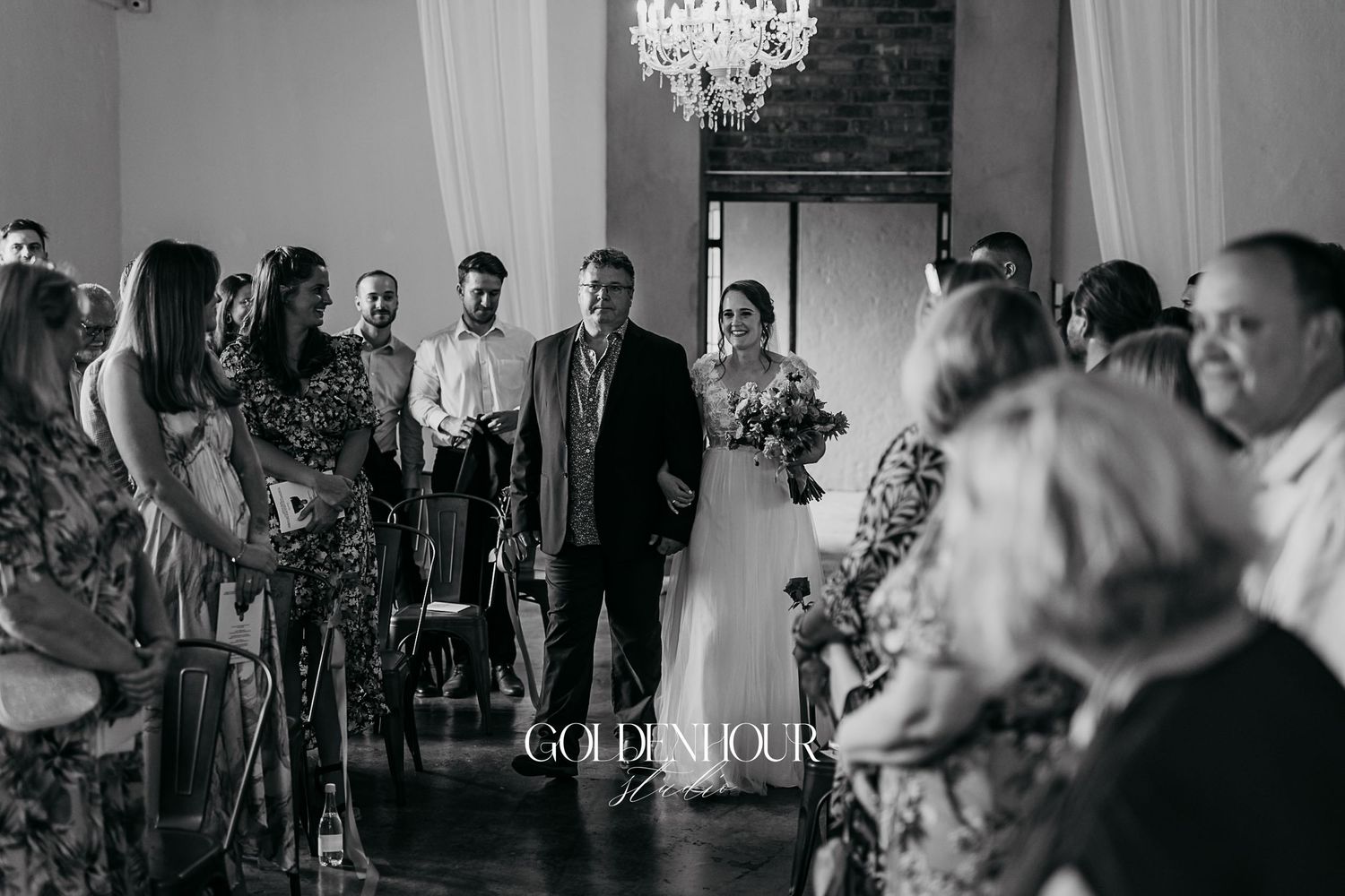 Black and white photo of bride walking down the aisle with her father at wedding ceremony.