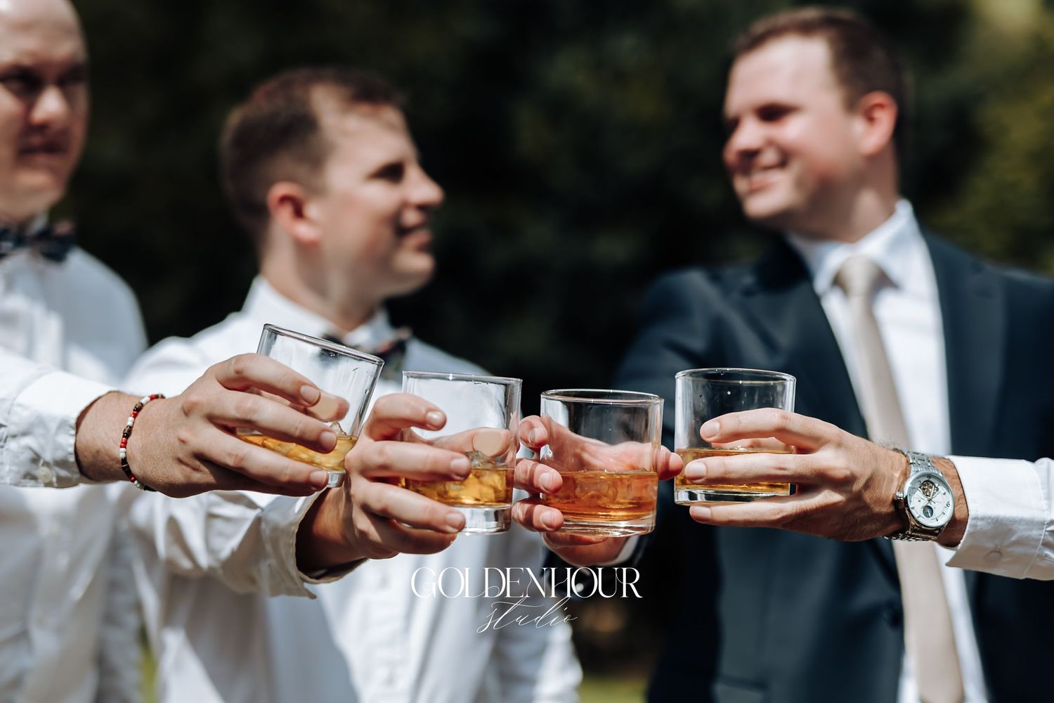Groomsmen toasting with glasses of whiskey outdoors at a wedding celebration.