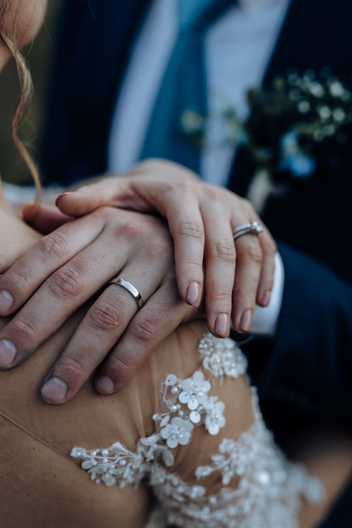 Close-up detail of wedding rings and lace dress fabric as couple holds hands.