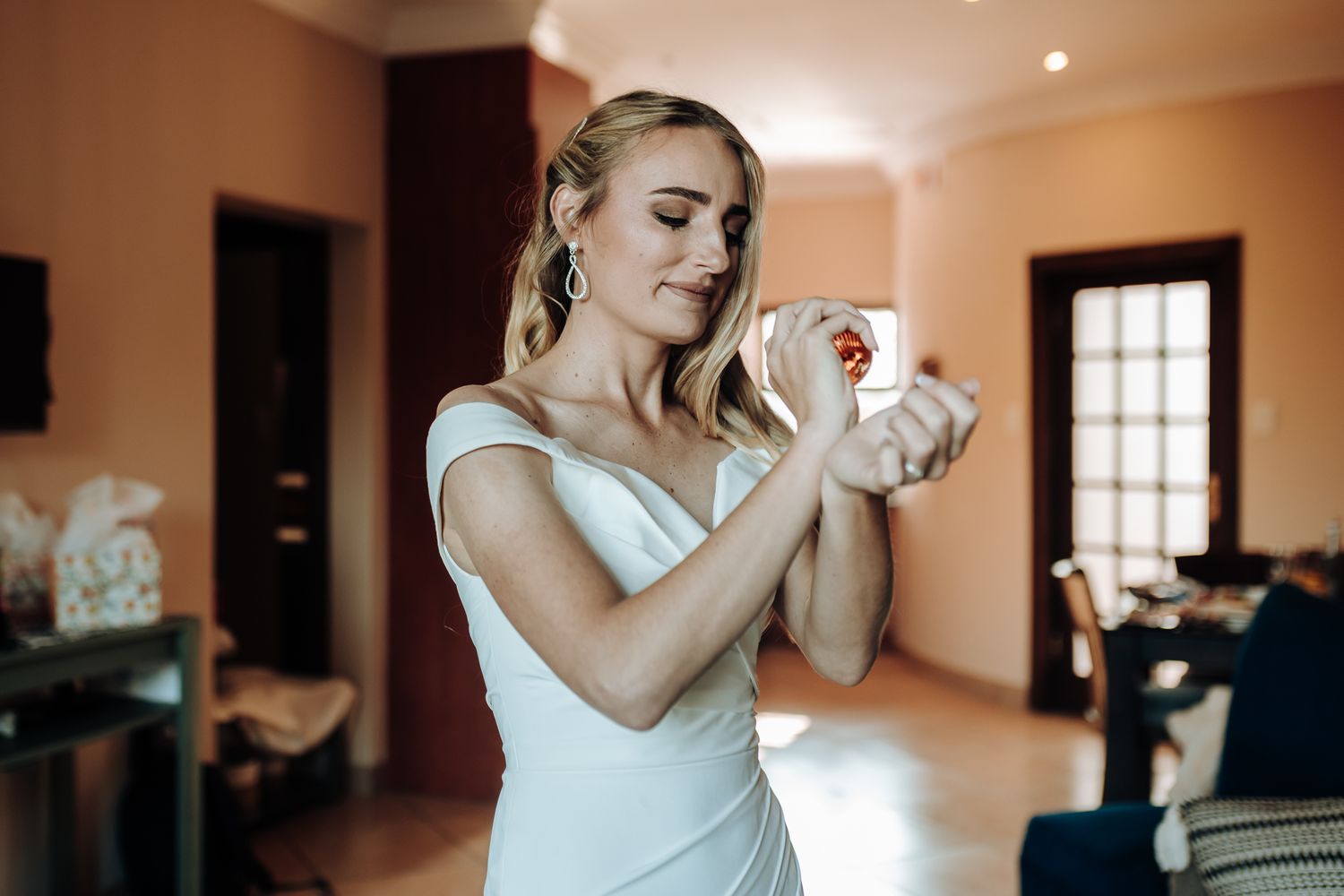 Bride spritzing perfume while getting ready in her elegant white gown.