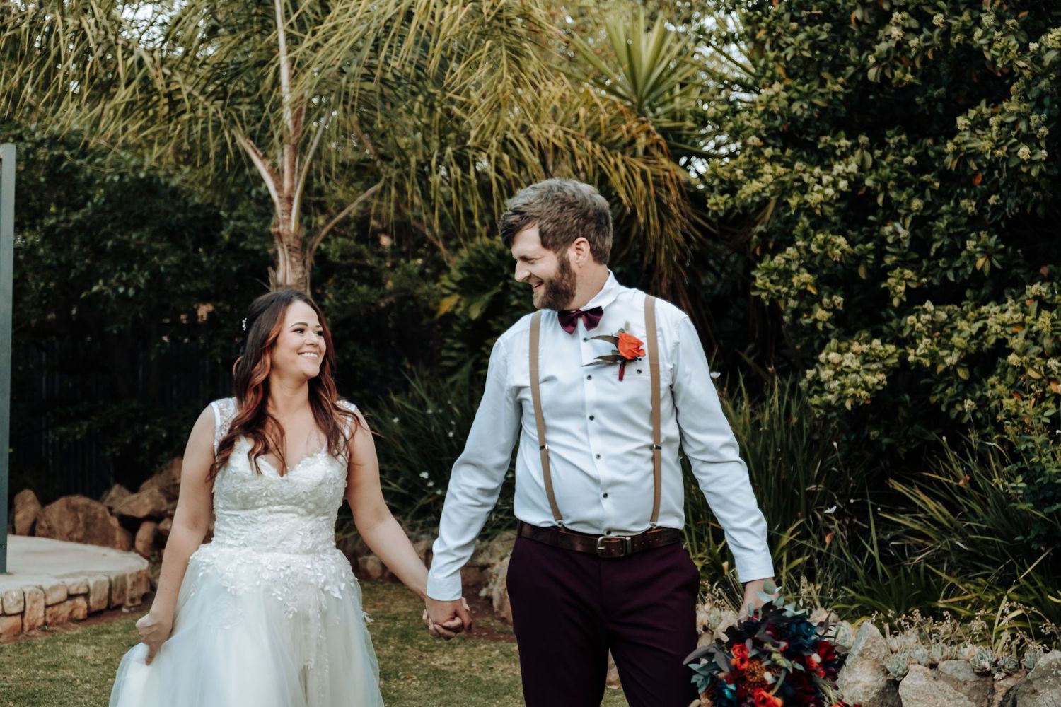 Couple sharing happy moment in garden with palm trees and floral decorations.