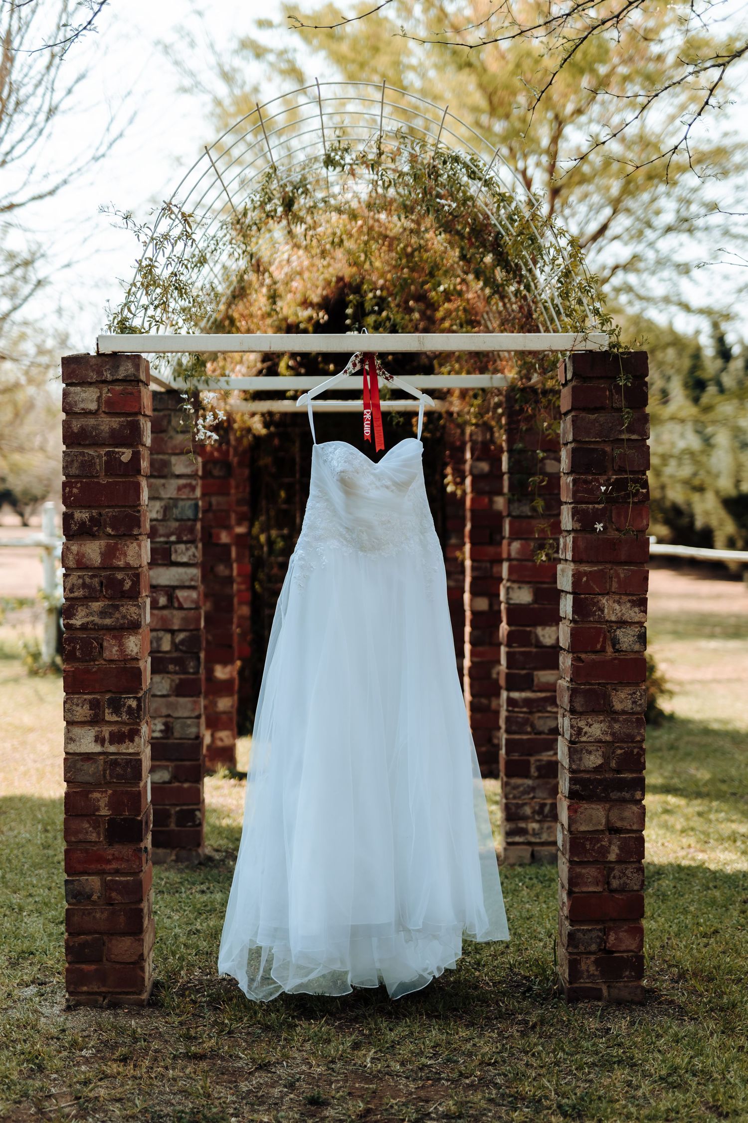 White wedding dress hanging on brick archway in outdoor garden setting.