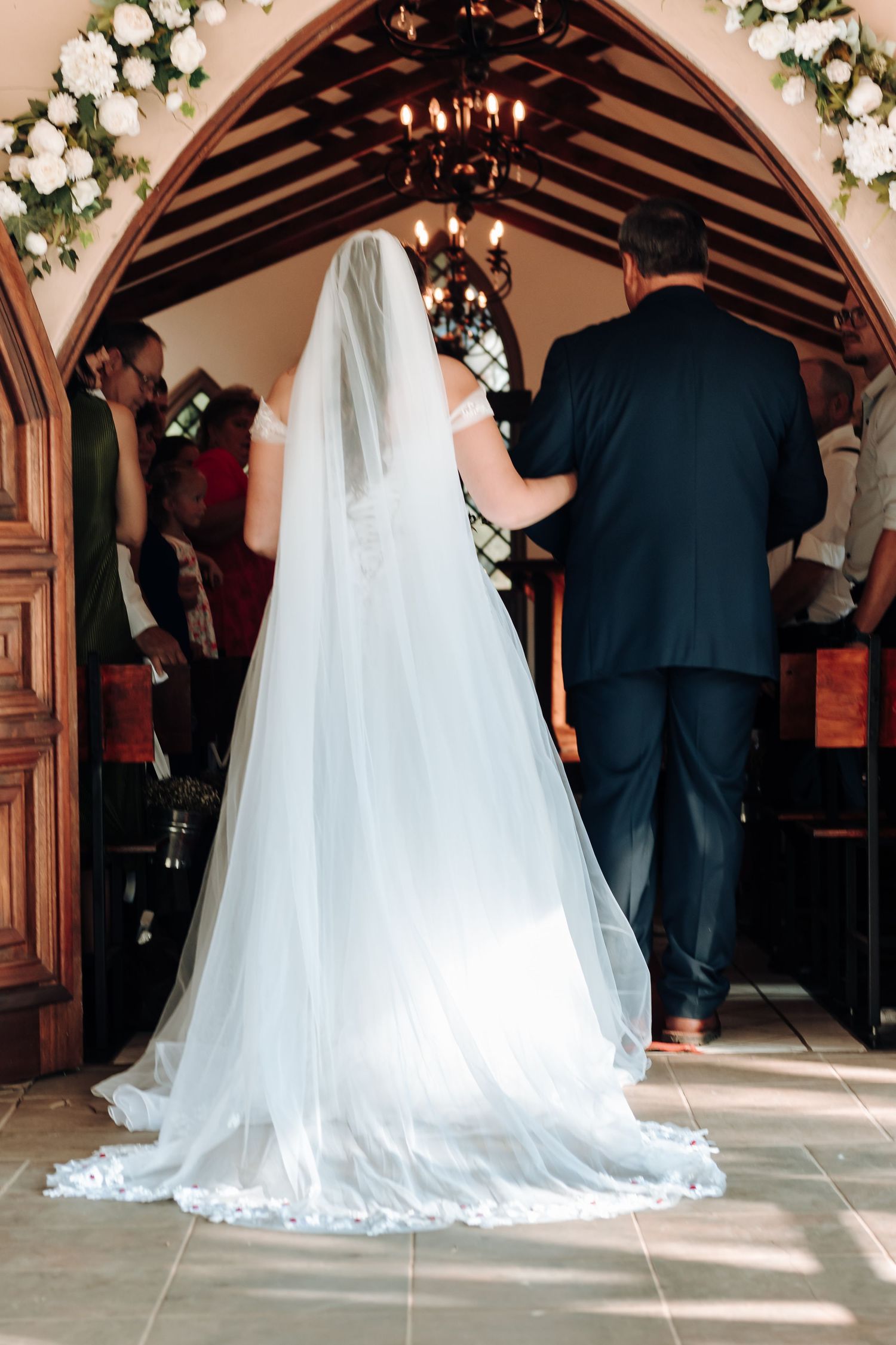 Back view of bride in flowing white gown entering through ornate wooden archway.