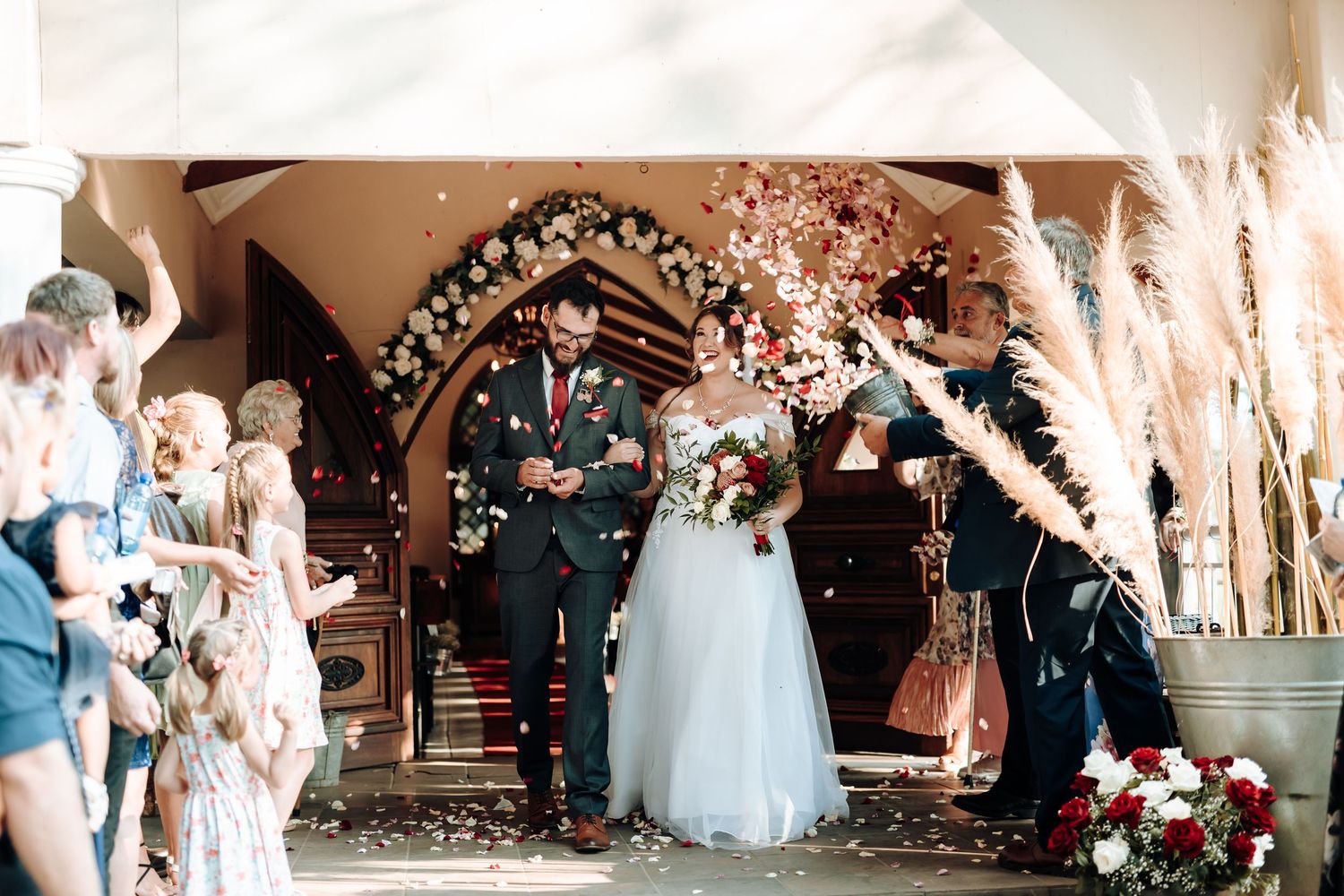 Newlyweds exit through floral arch during outdoor wedding celebration.