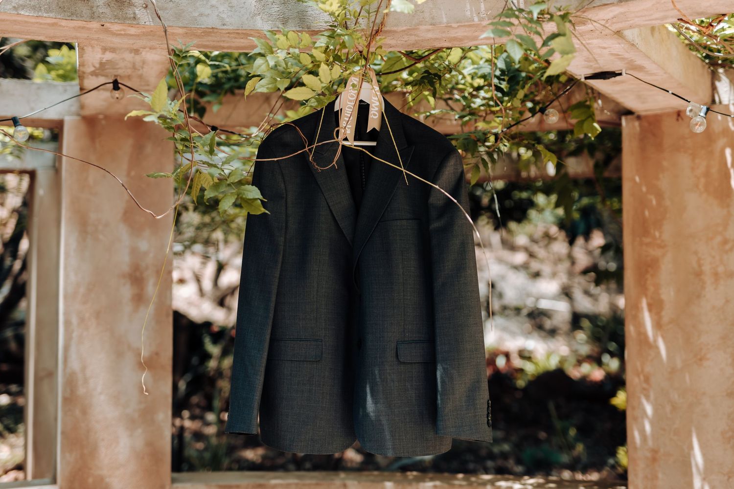 Black suit jacket hanging on wooden structure in outdoor setting.