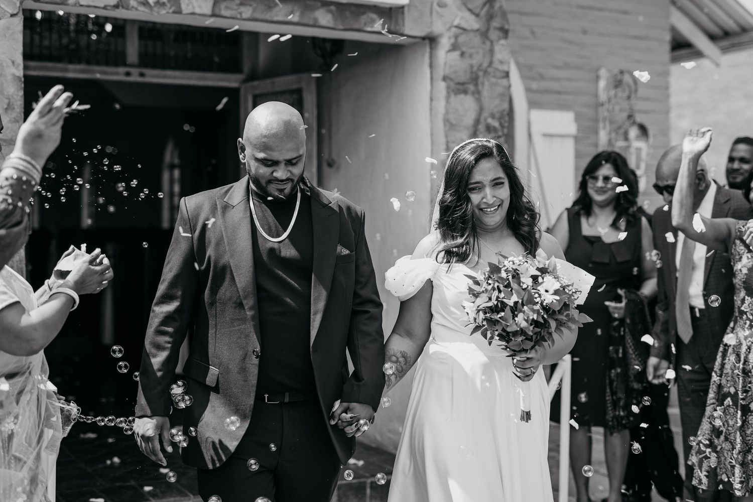 Wedding couple exiting venue while guests throw confetti in celebration.