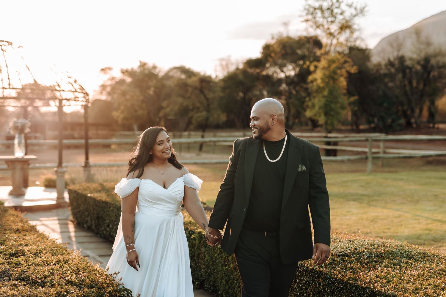 Wedding couple walks hand in hand during golden hour at a rustic outdoor venue.