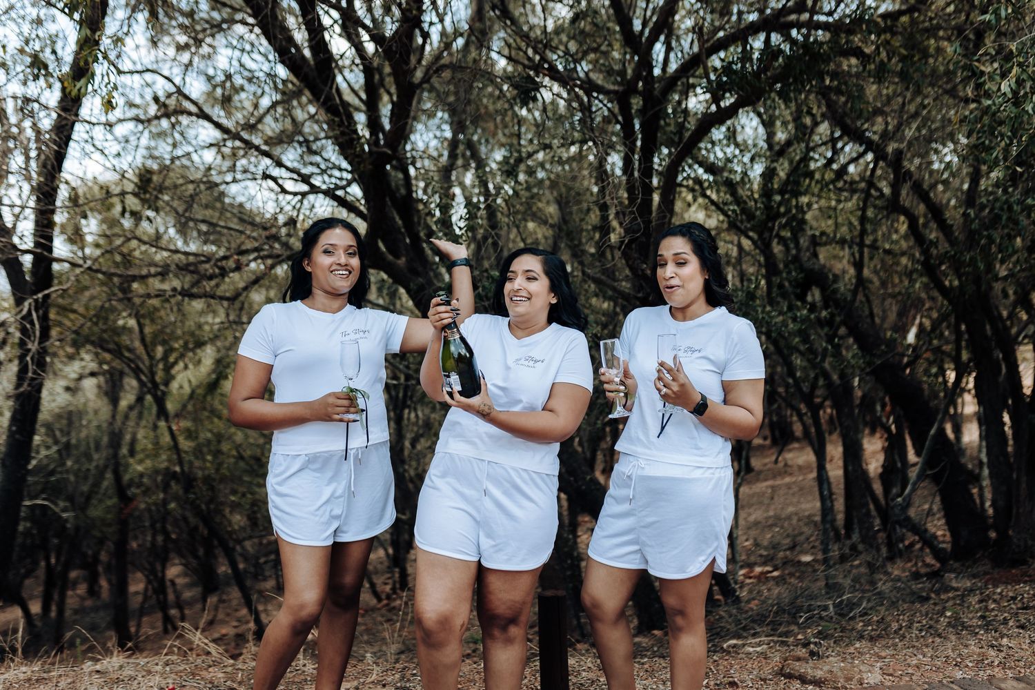 Group wearing matching white outfits laughing together in a wooded setting.