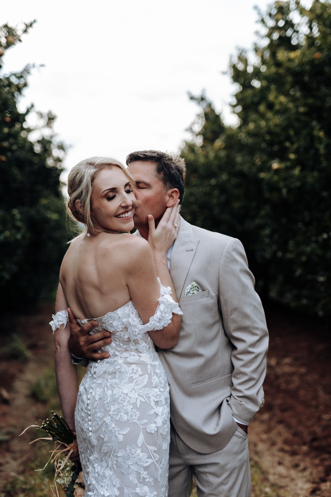 Intimate wedding portrait showing detailed lace dress in orchard setting.
