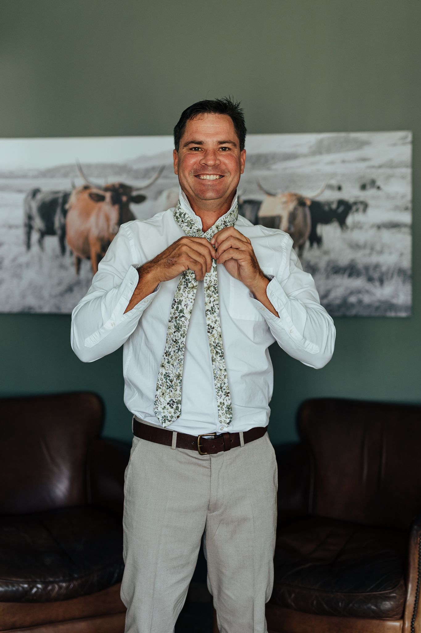 Person adjusting floral tie while wearing white dress shirt and light colored pants.