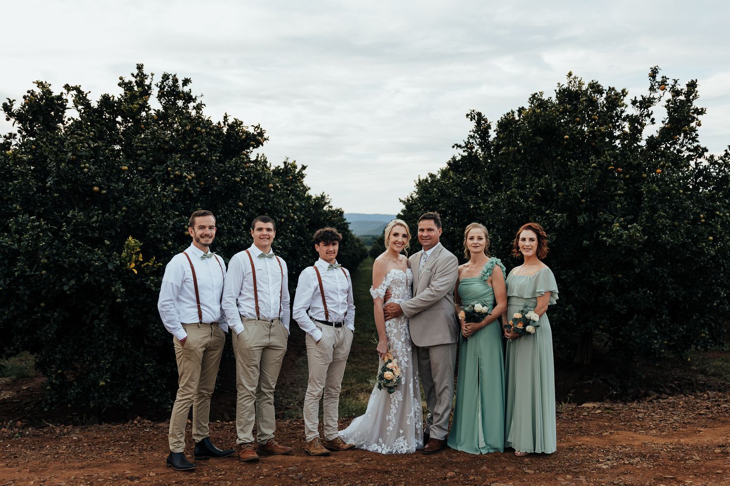 Wedding party poses together in mint green dresses and khaki suits against an orchard backdrop.