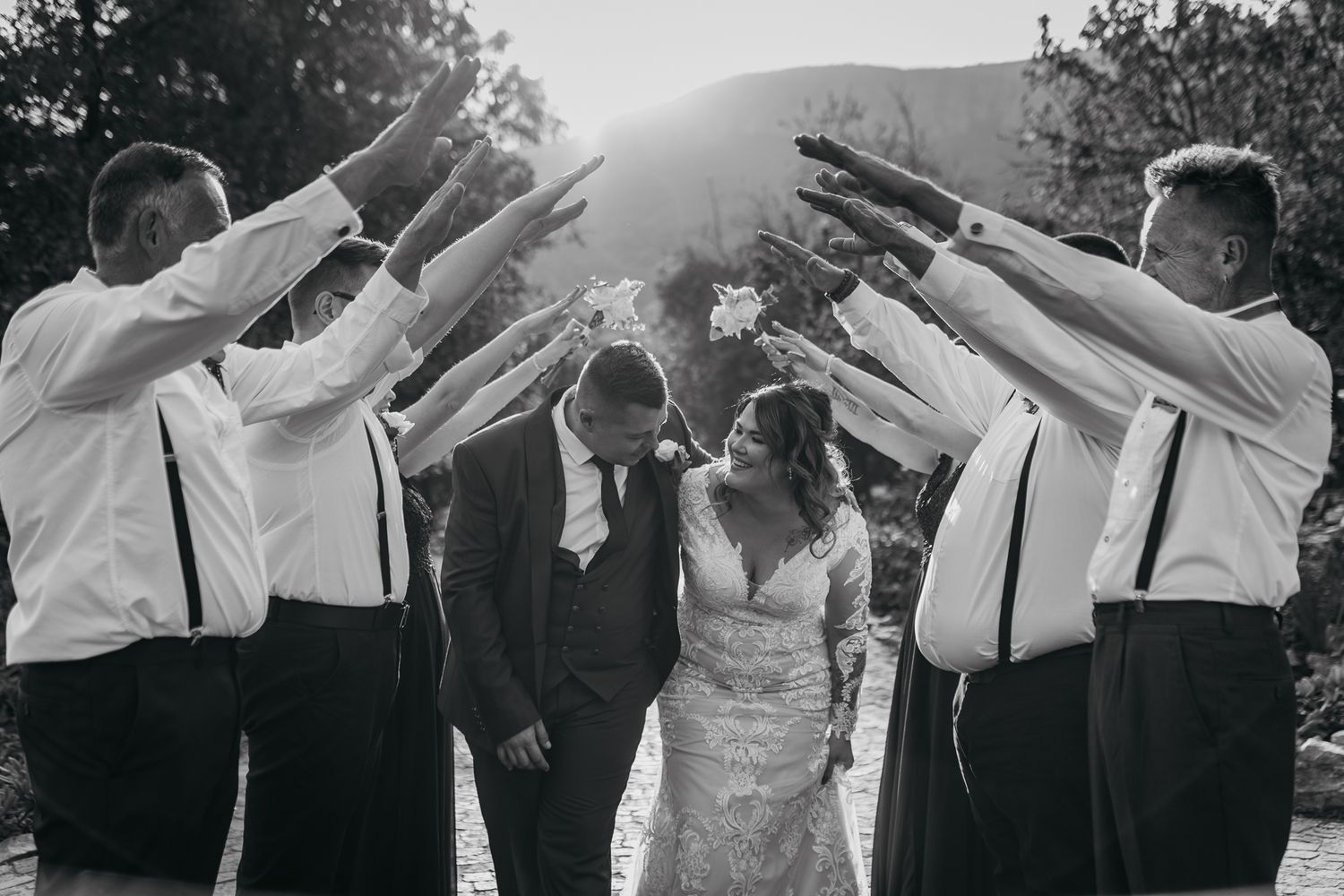 Wedding party forms an arch with raised arms for the newlyweds to walk through during outdoor ceremony.