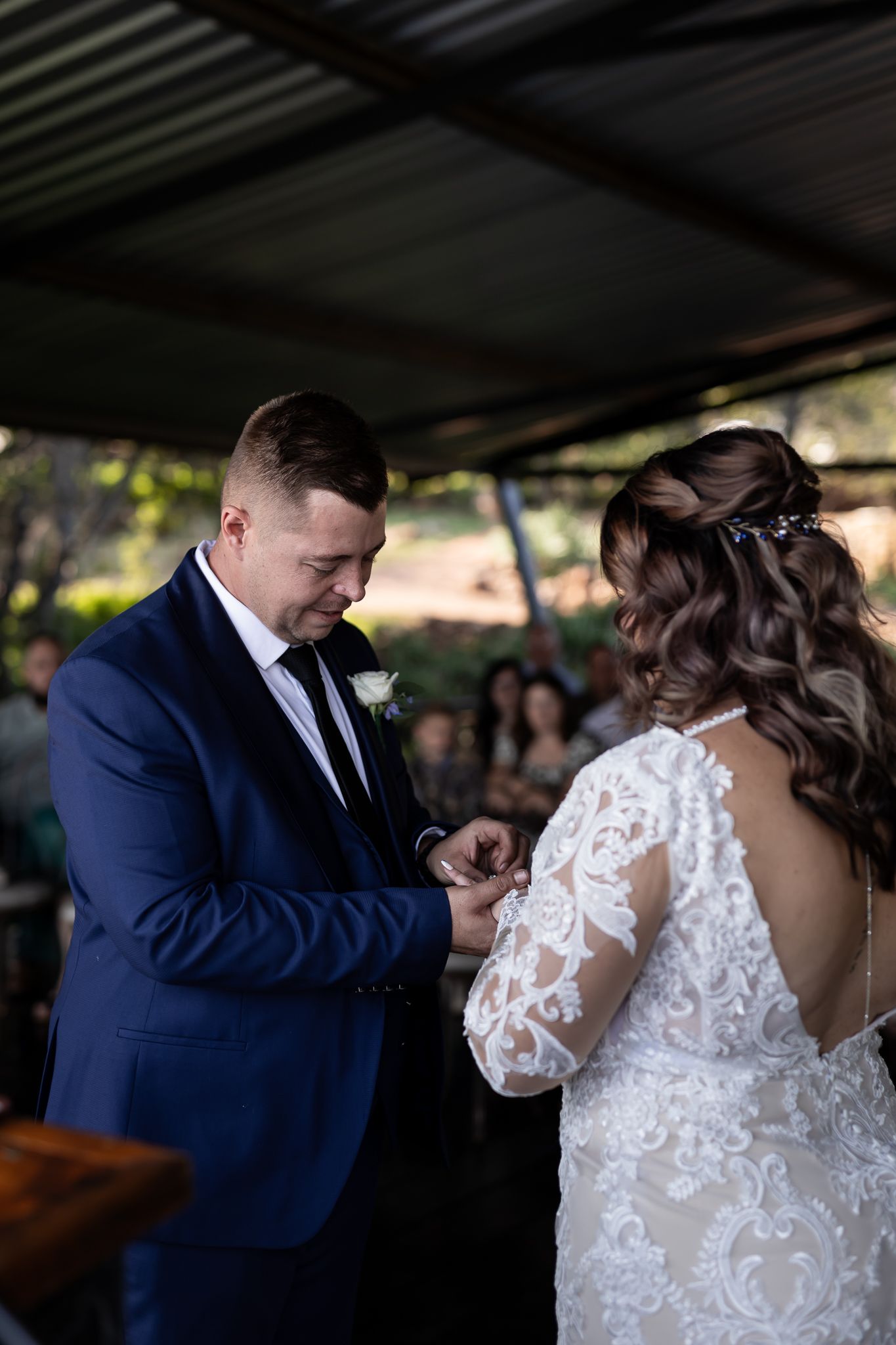 Groom placing ring on bride's finger during outdoor wedding ceremony.