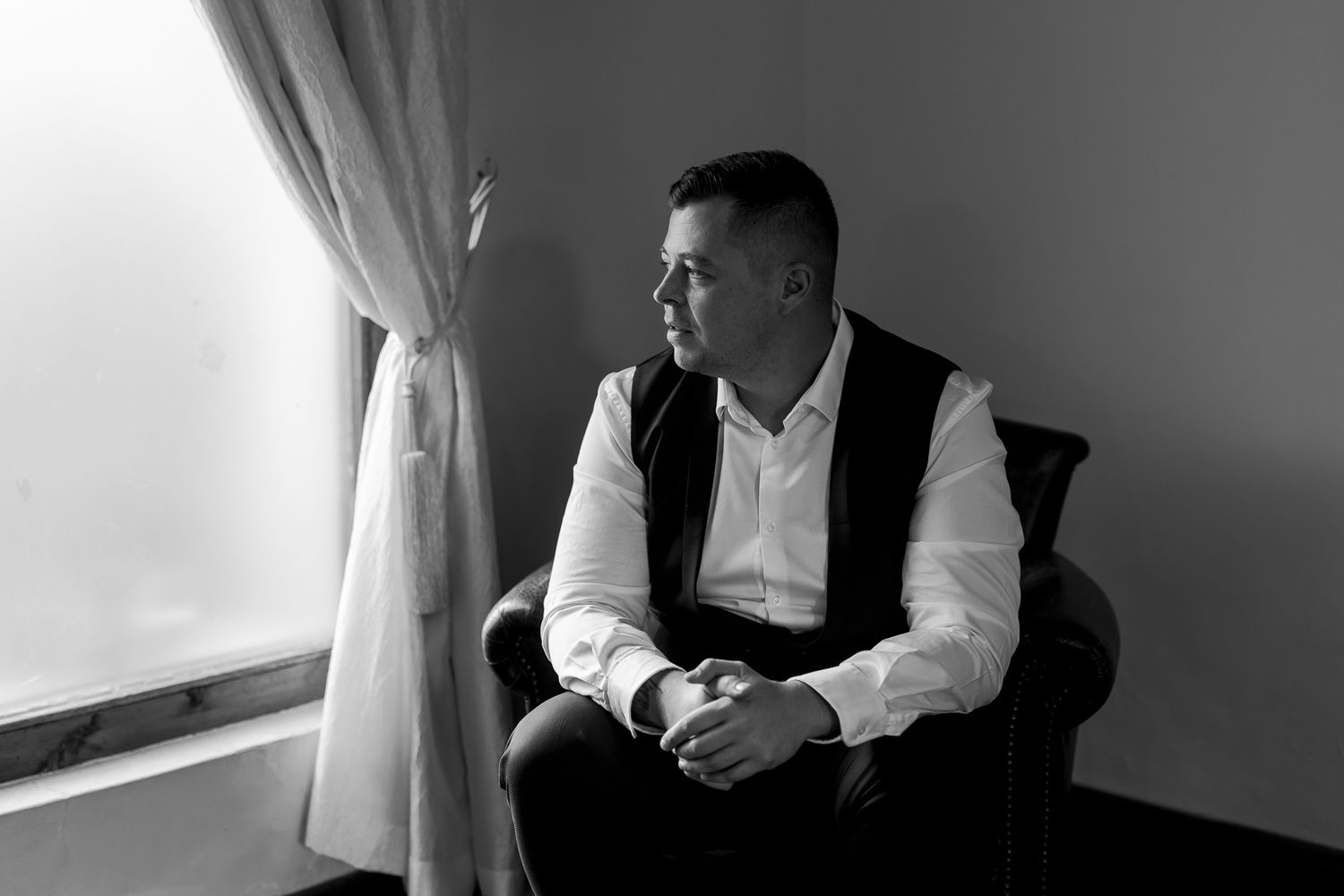 Black and white portrait of person seated by window in formal attire.