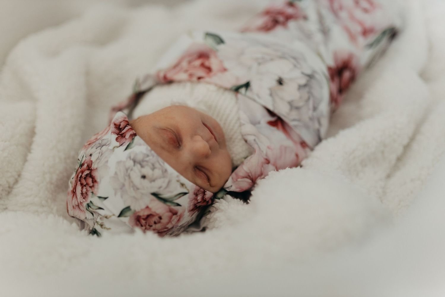 Sweet floral-wrapped baby nestled in white bedding with a delicate rose pattern.