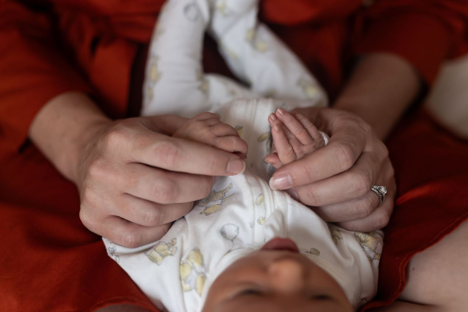 A close-up view shows gentle hands holding a tiny newborn baby wrapped in white fabric.