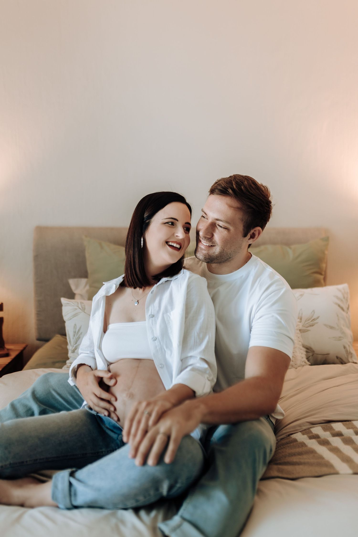 A couple in white shirts laughing together while relaxing on a comfortable bed.