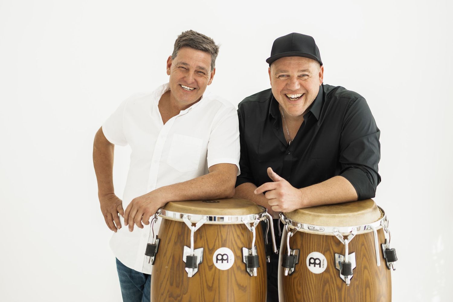 Two people in black shirts pose and smile while playing congas together during a percussion performance.