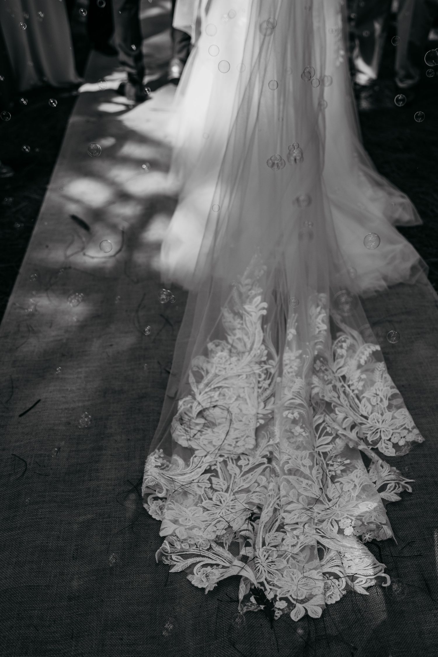 Close-up view of delicate lace details on a white wedding dress hem against a dark floor.