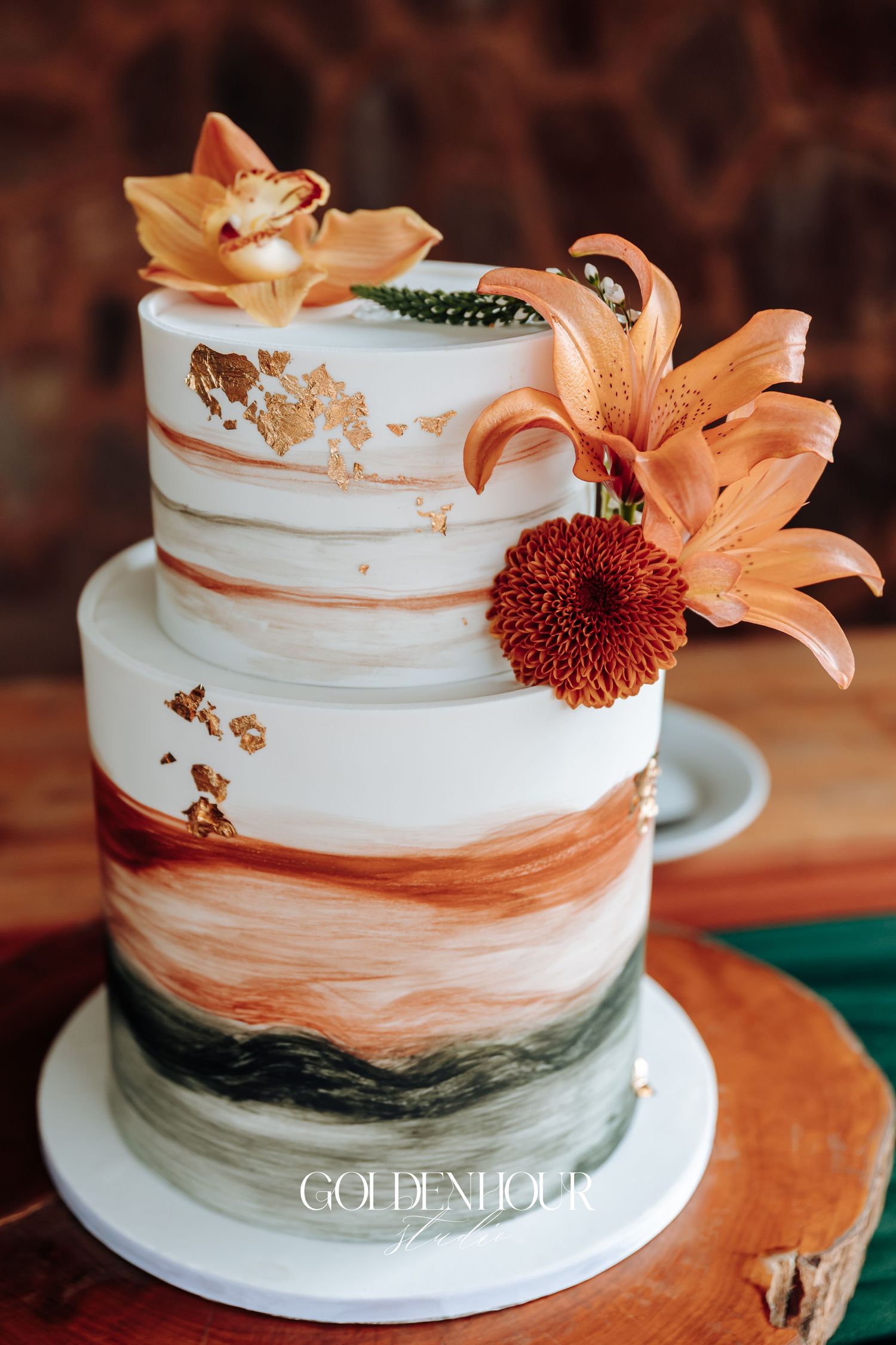White wedding cake decorated with orange lilies and copper-colored brushstroke design.