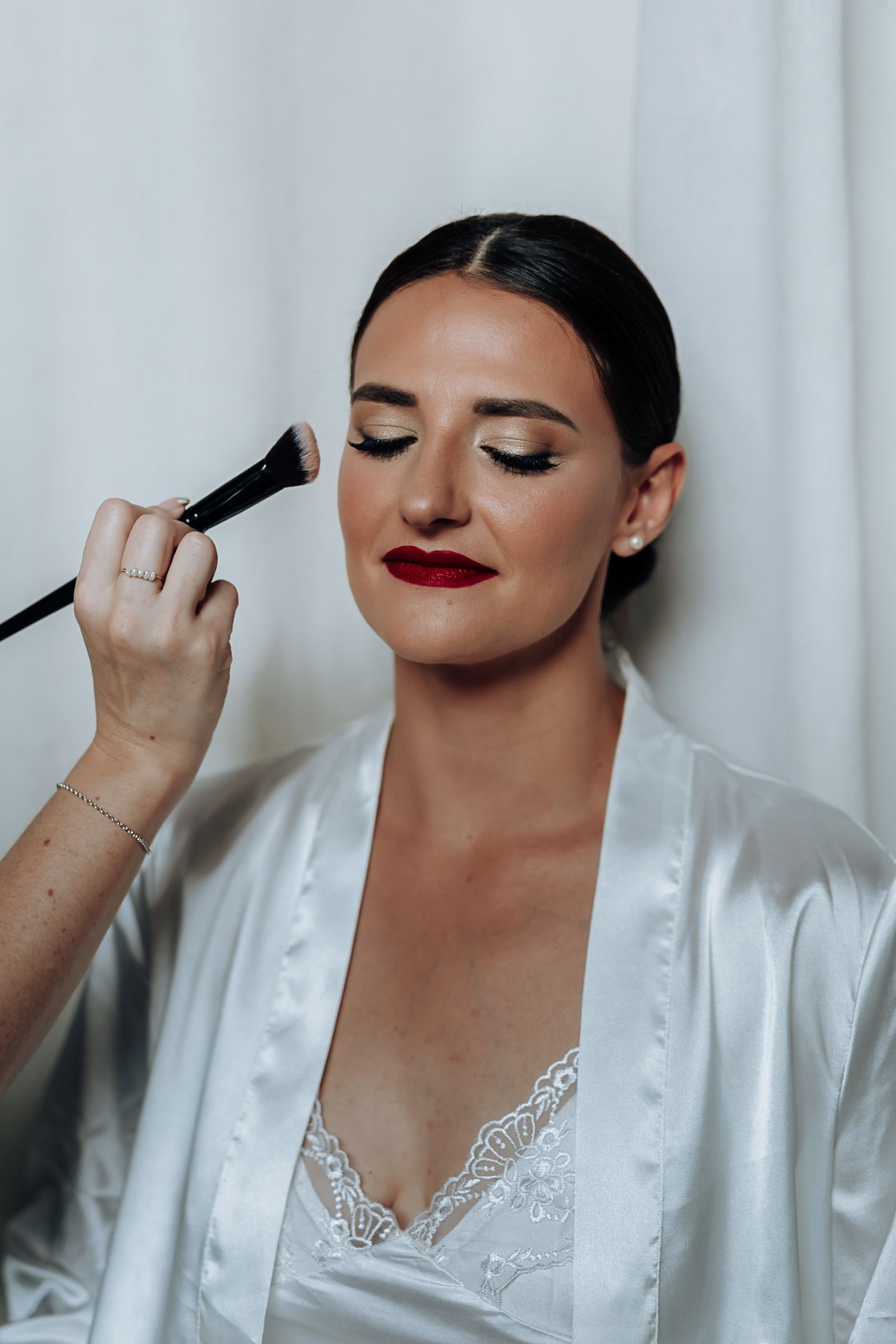 A series of four photos showing makeup application with brushes on someone wearing a white lace-trimmed robe.