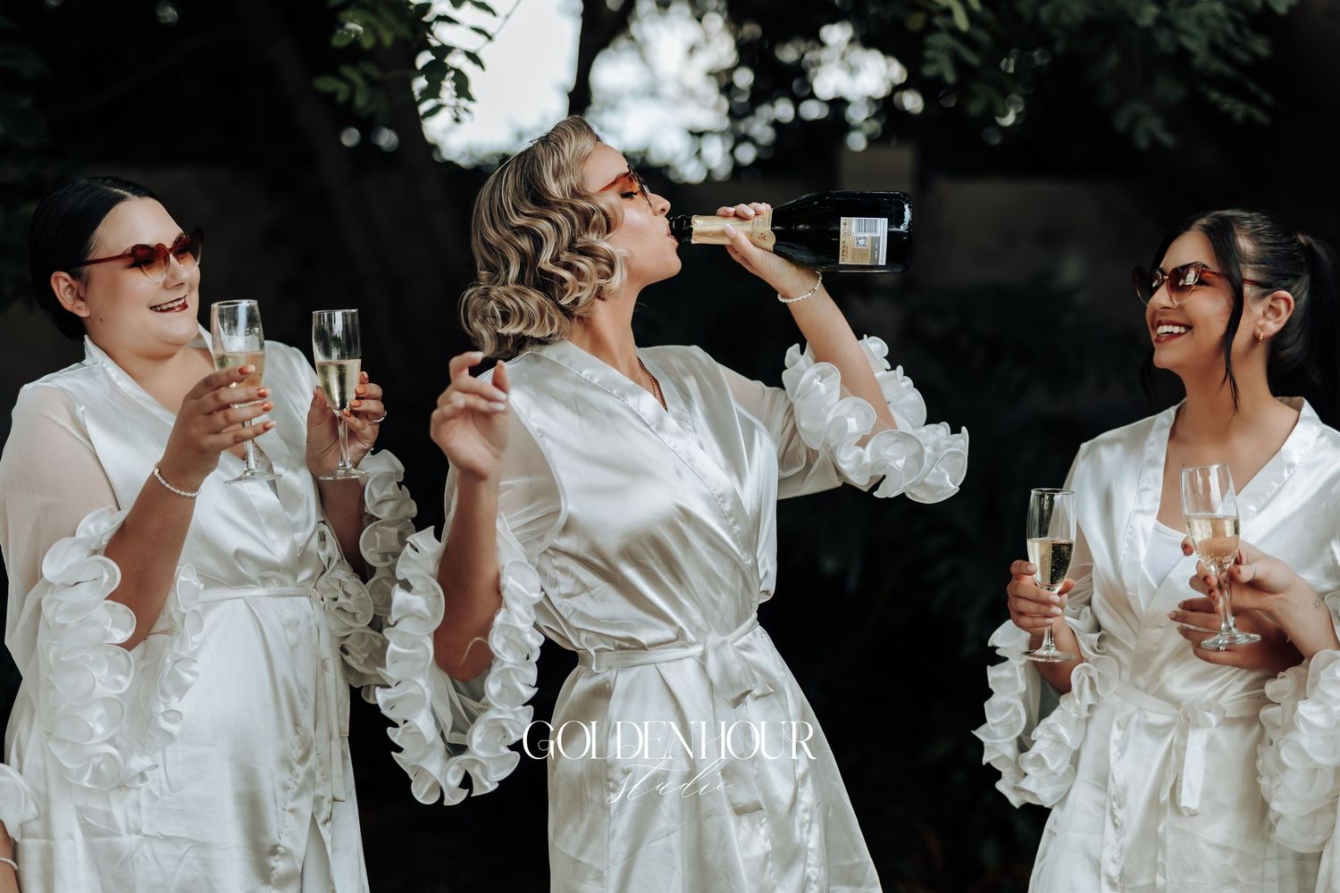 Wedding party members in white silk robes toast with champagne glasses.