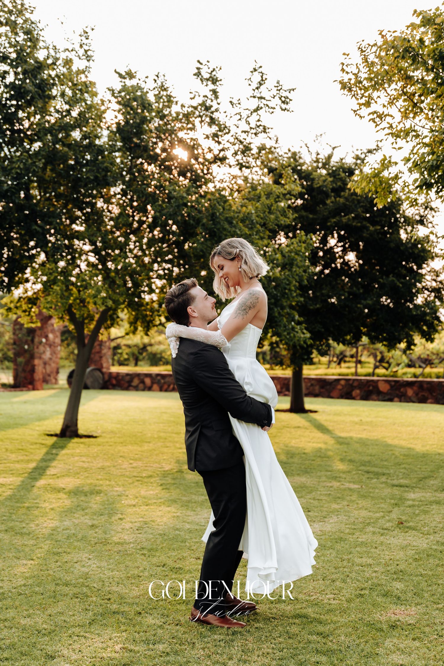 Joyful wedding couple dances and twirls on a grassy lawn at golden hour.