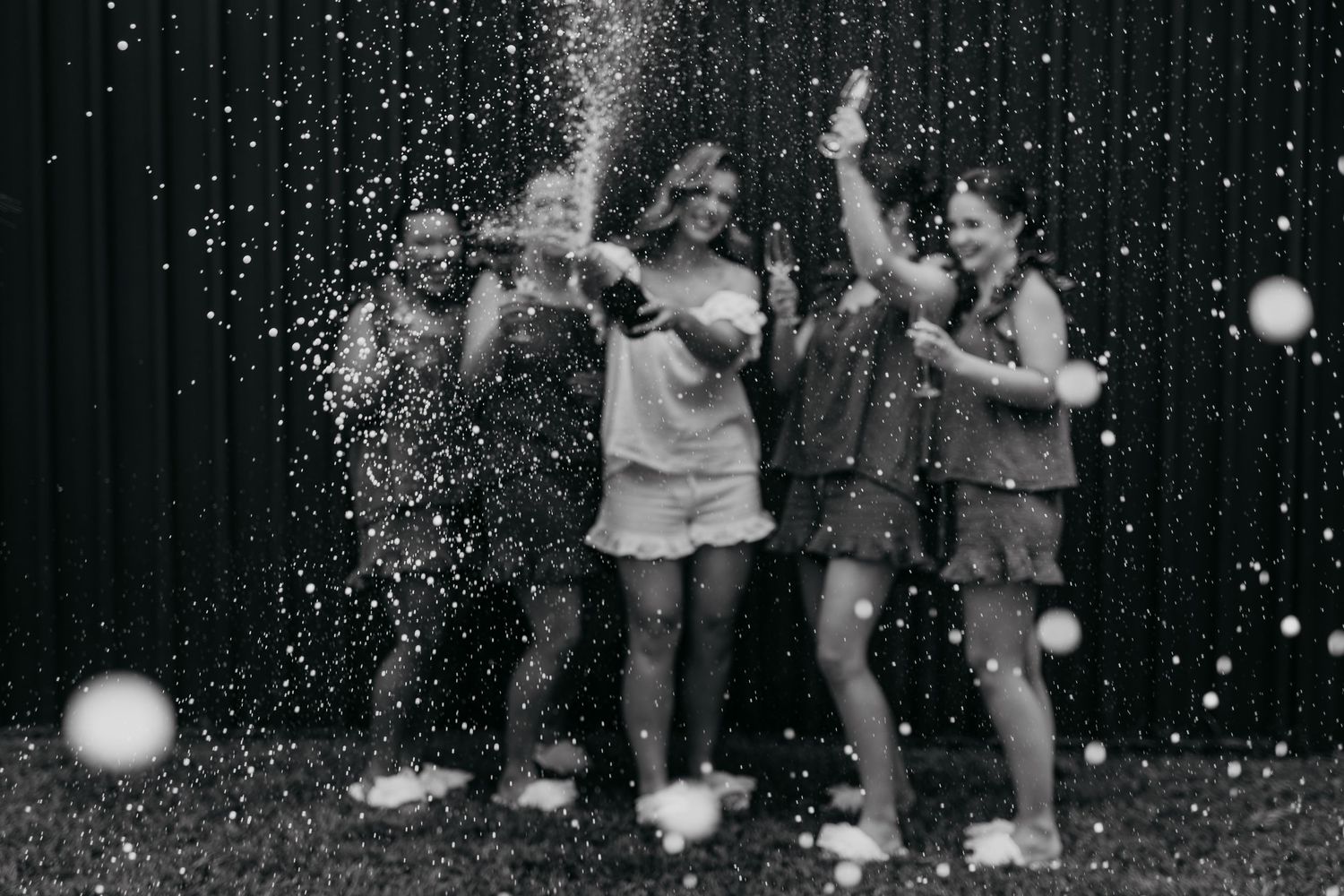 A group celebrating with champagne spraying in the air against a dark background with sparkles.