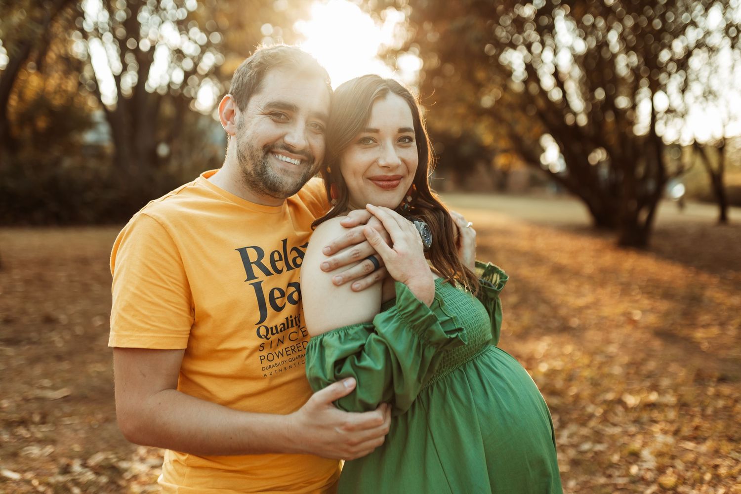 Couple wearing green and yellow shirts share a joyful moment together in a golden-lit autumn setting.