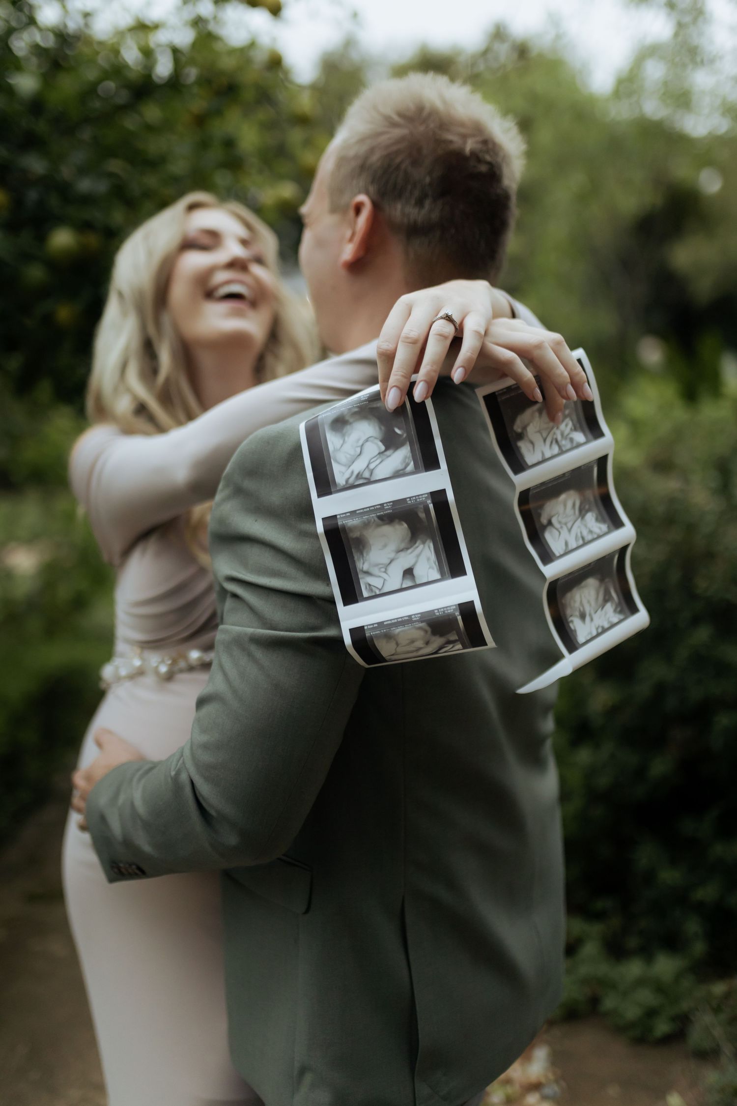 A couple holding sonogram photos during an emotional outdoor pregnancy announcement.