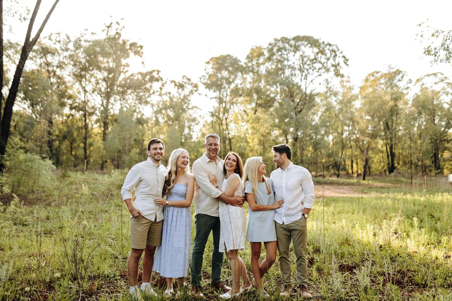 A cheerful gathering of people in light-colored clothing walking through a natural outdoor setting at sunset.