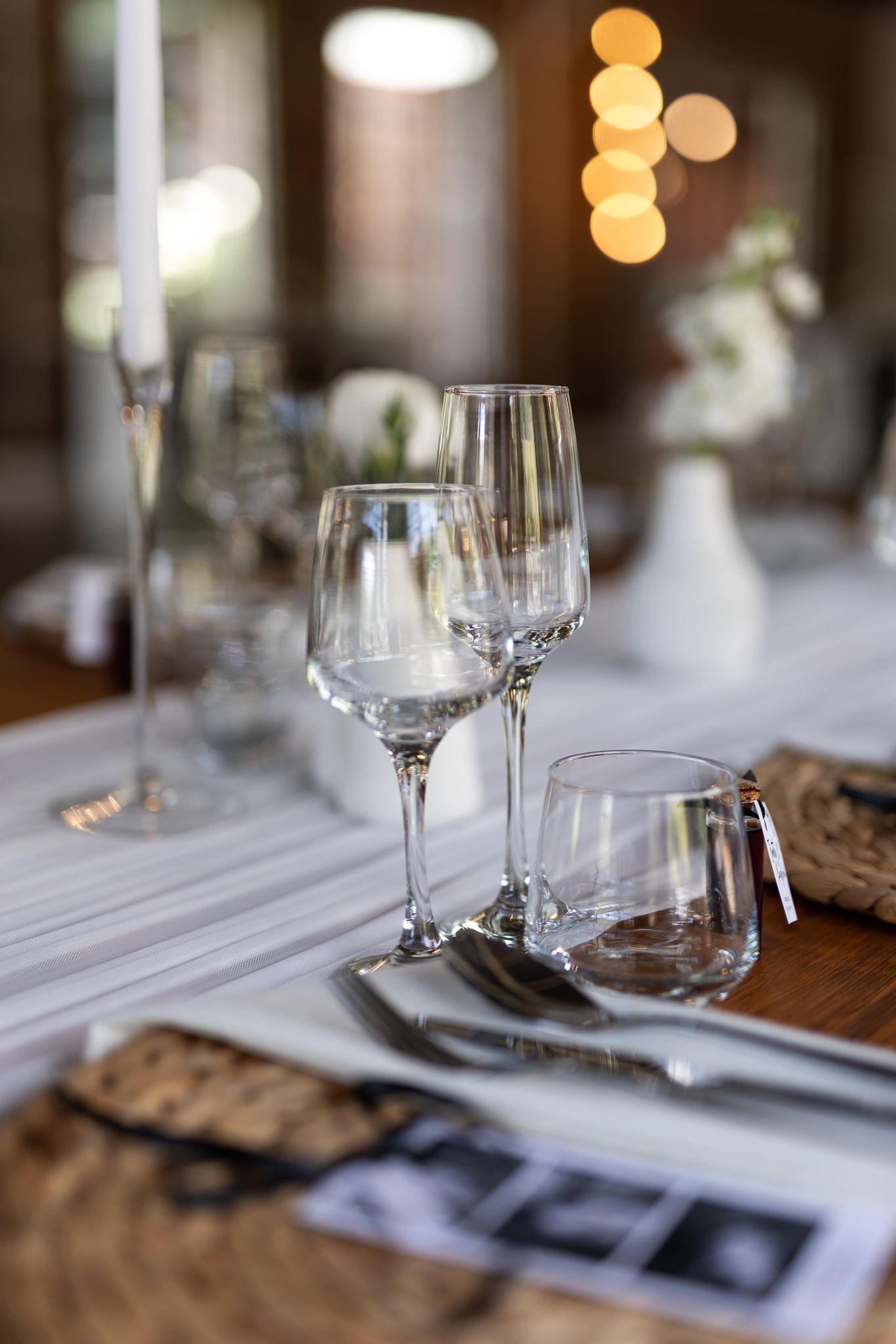 Elegant wine glasses and place settings on a wooden table with bokeh lighting in the background.