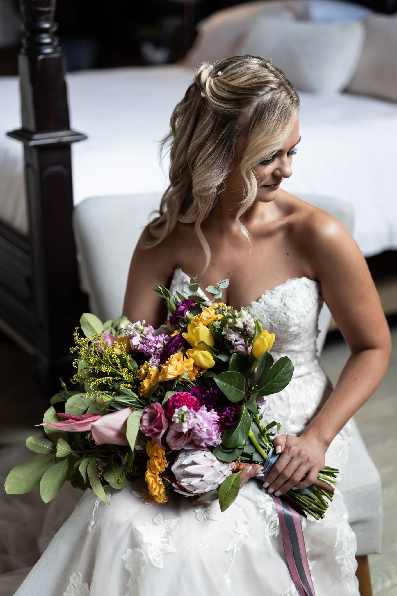 A bride in a white lace gown holds a vibrant bouquet featuring yellow, purple, and pink flowers.