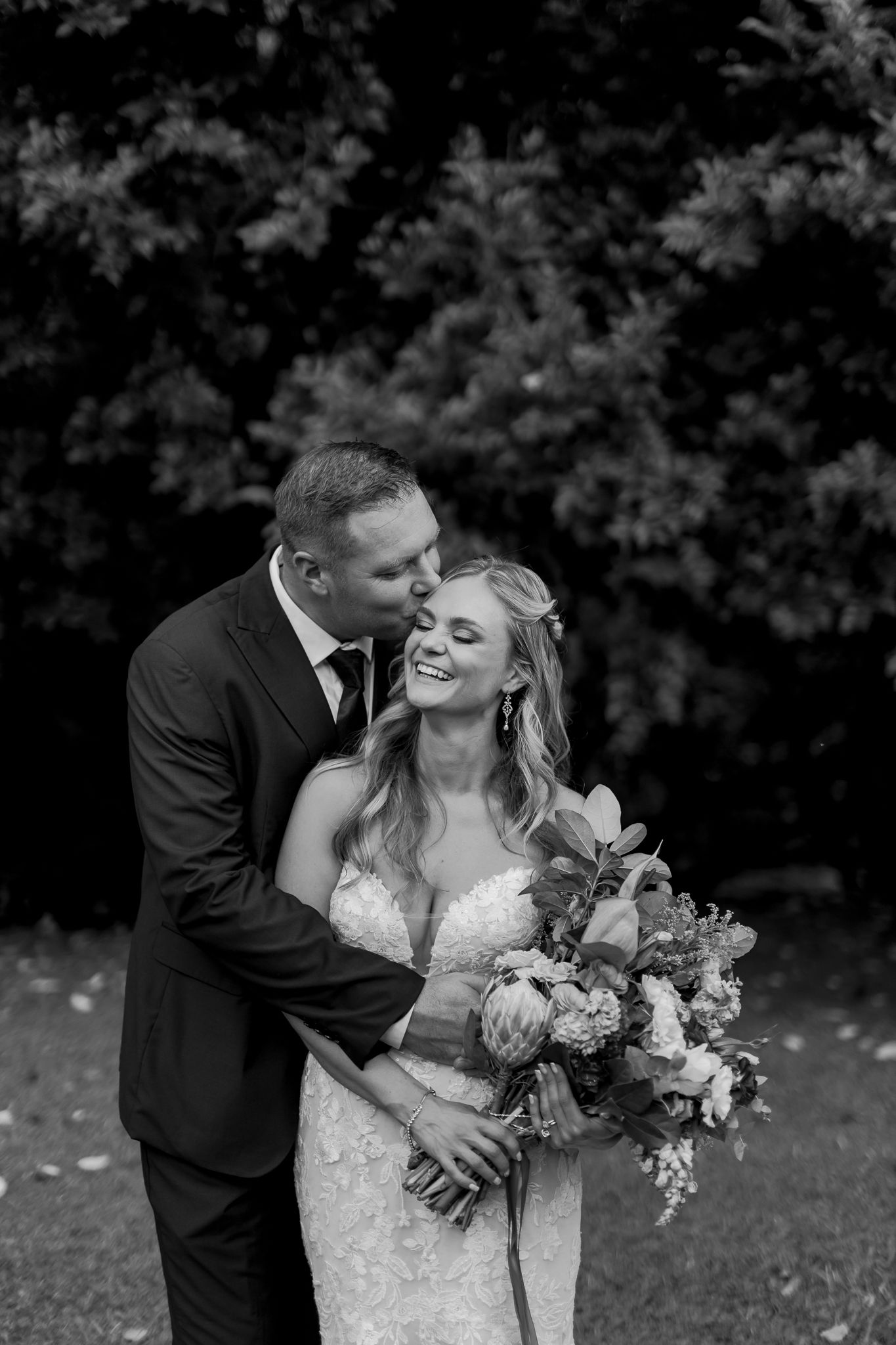 Black and white portrait of newlyweds sharing intimate moment with bride holding floral bouquet.