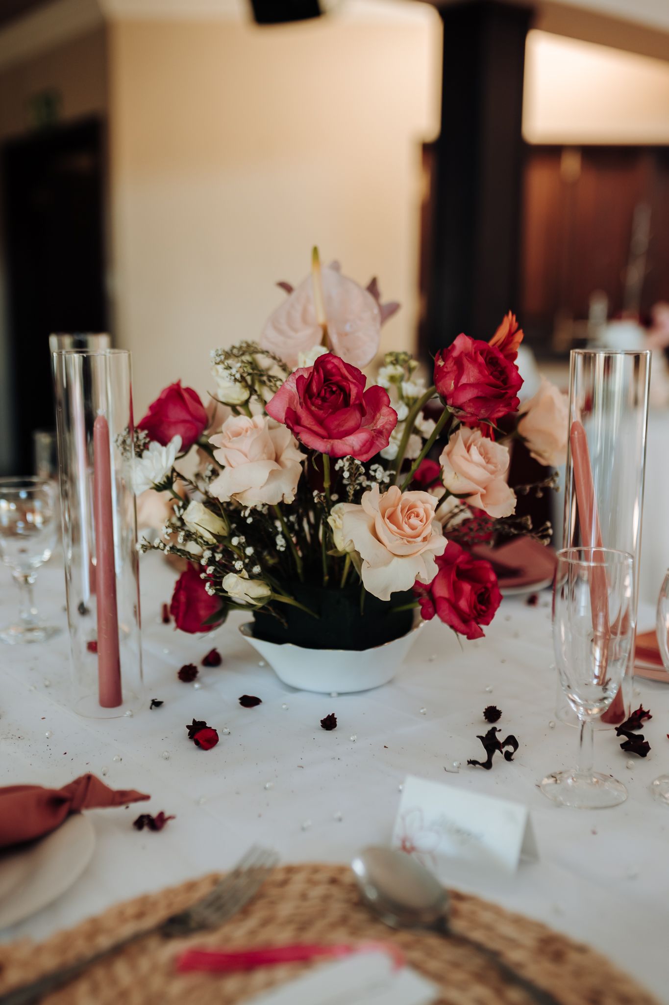 Mixed rose centerpiece with pink and red blooms in white vase surrounded by champagne glasses.