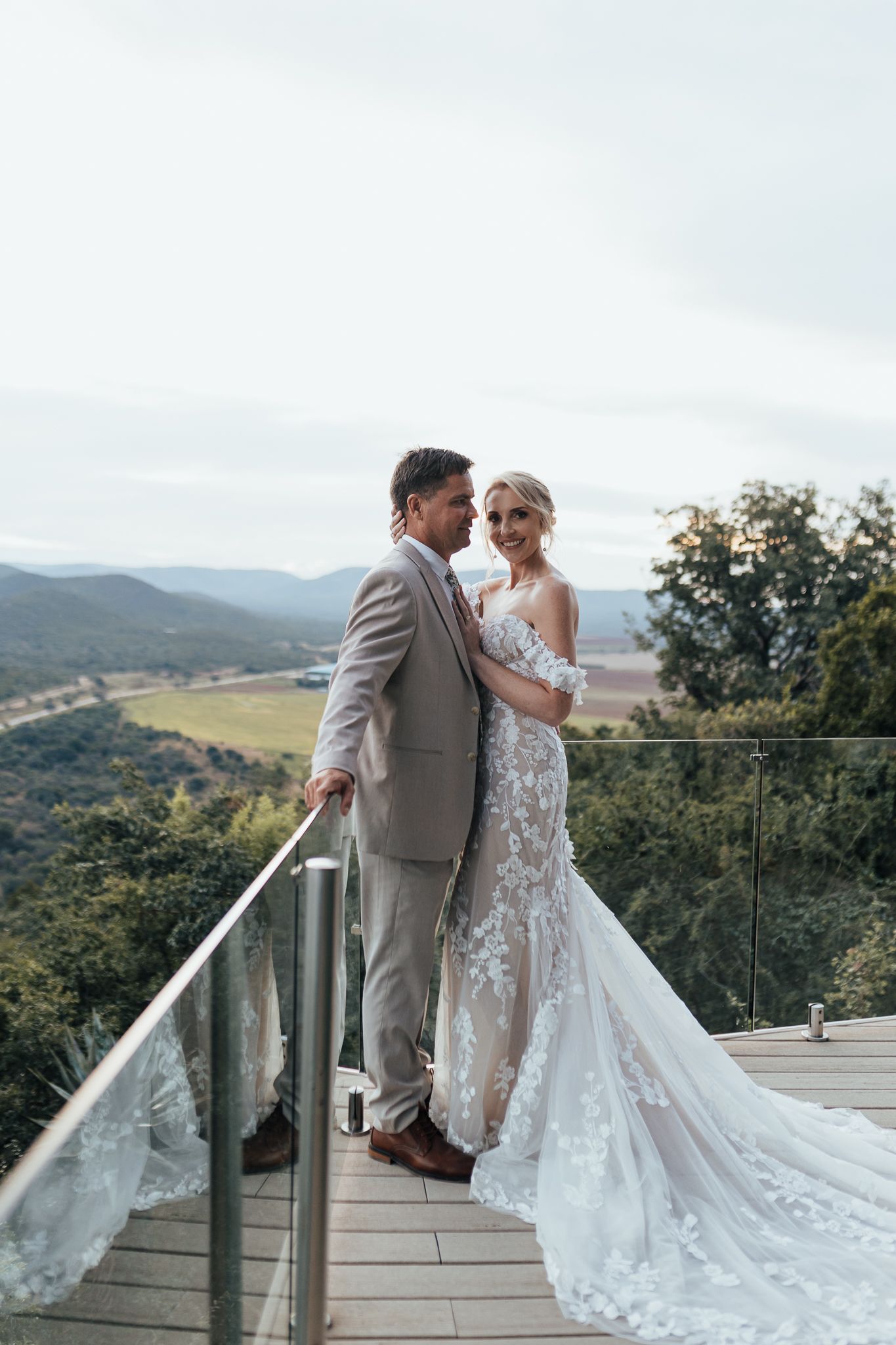 Wedding couple poses on a scenic mountain deck overlook with her detailed lace gown flowing.