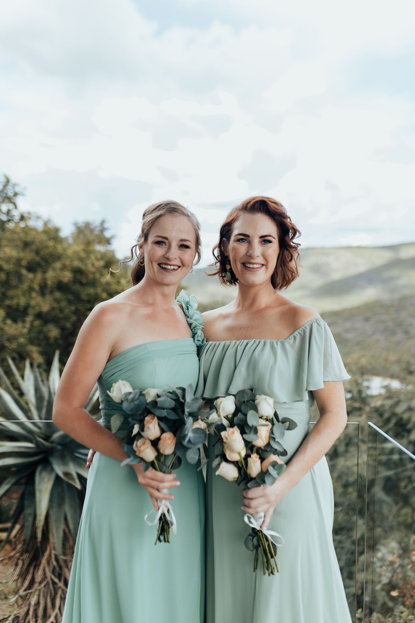 Two bridesmaids in mint green dresses hold matching bouquets while posing outdoors.