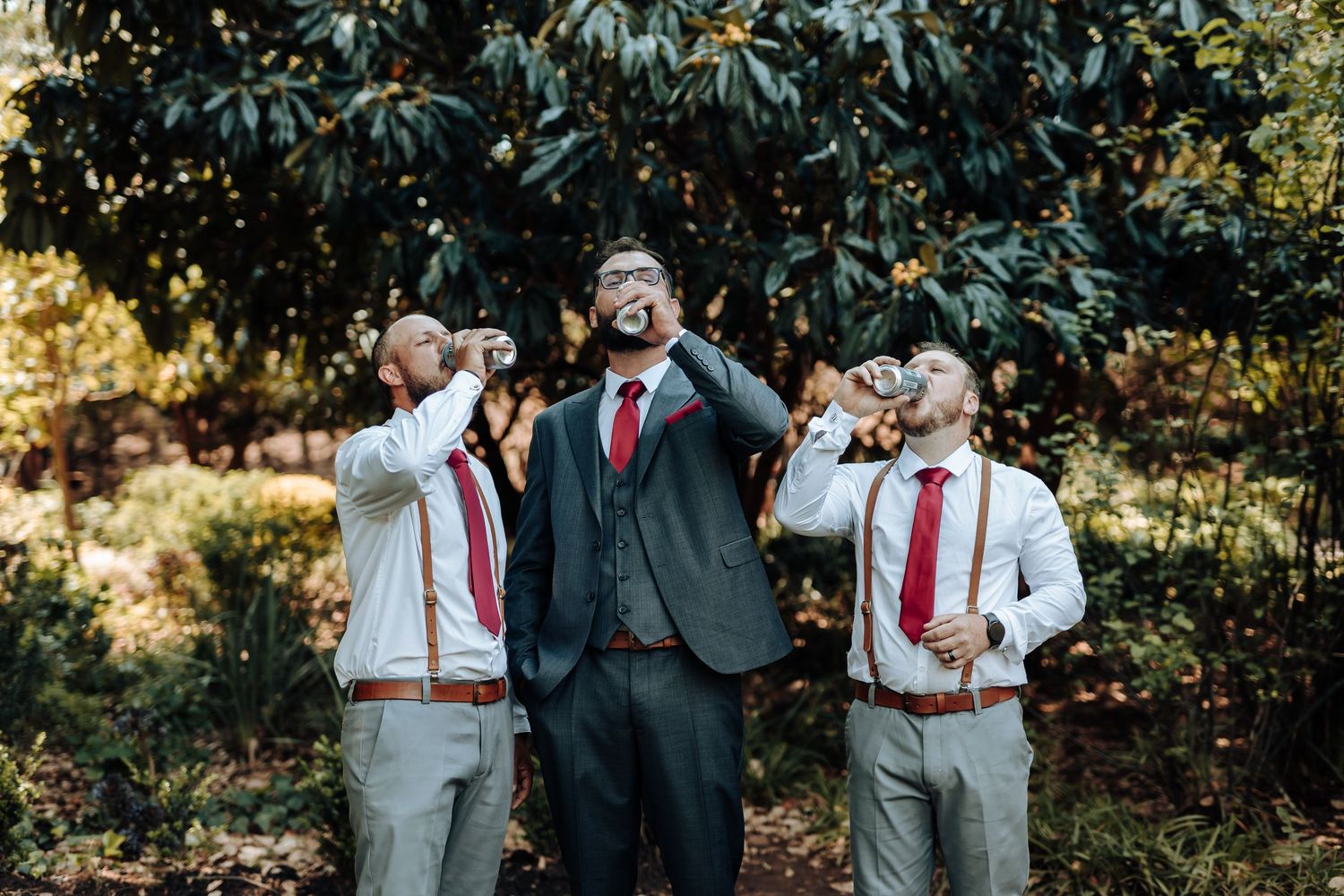 Wedding party members take celebratory drinks together in an outdoor garden setting.