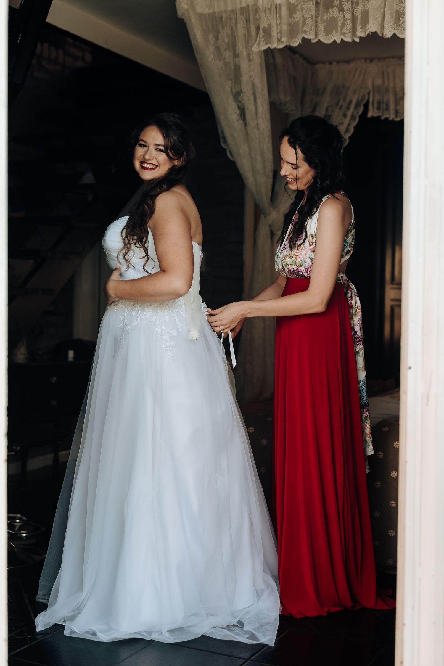 Wedding preparation scene with a bride in white gown and attendant in red dress.