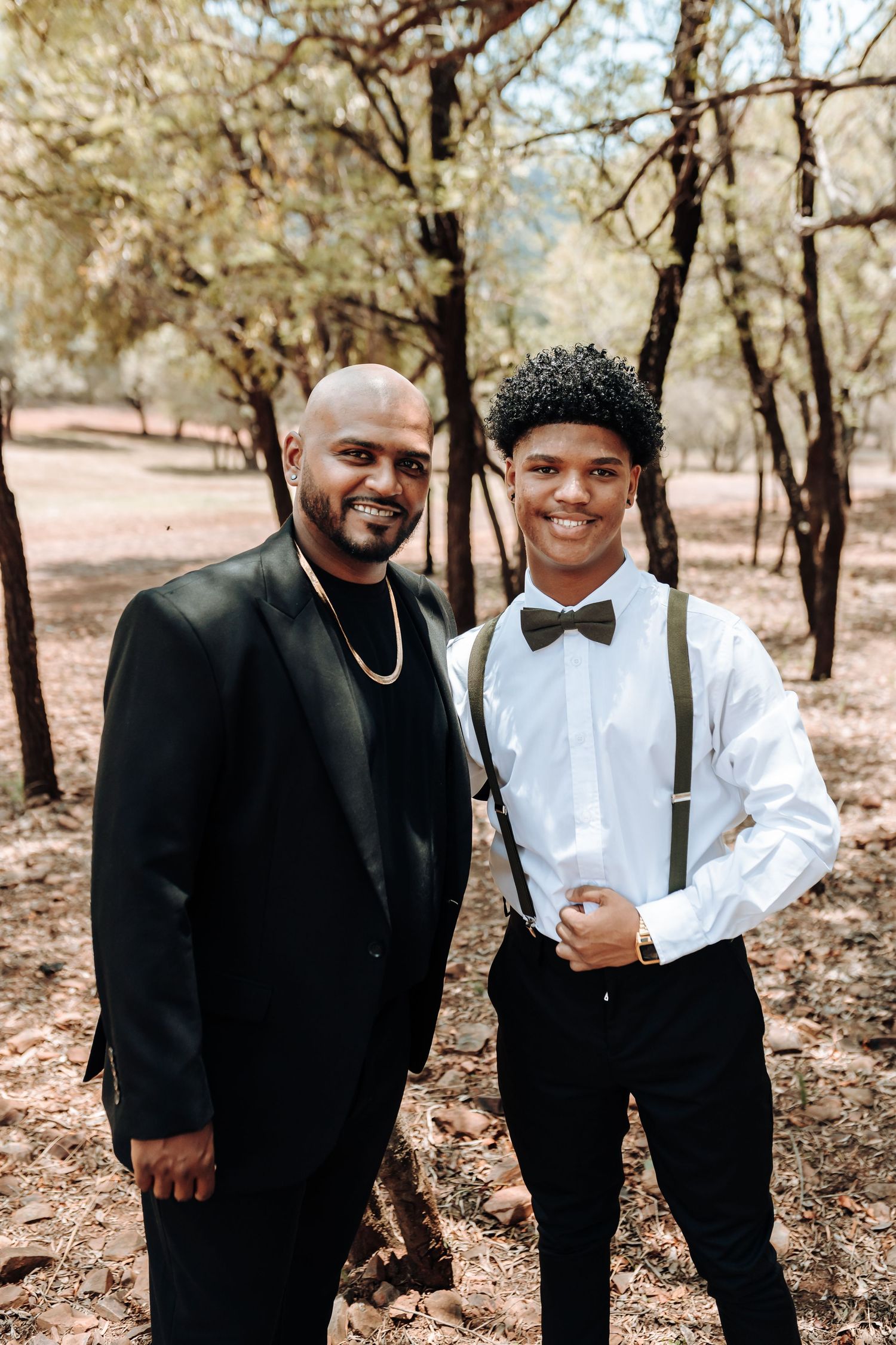 Two people in contrasting formal attire standing together in wooded setting.