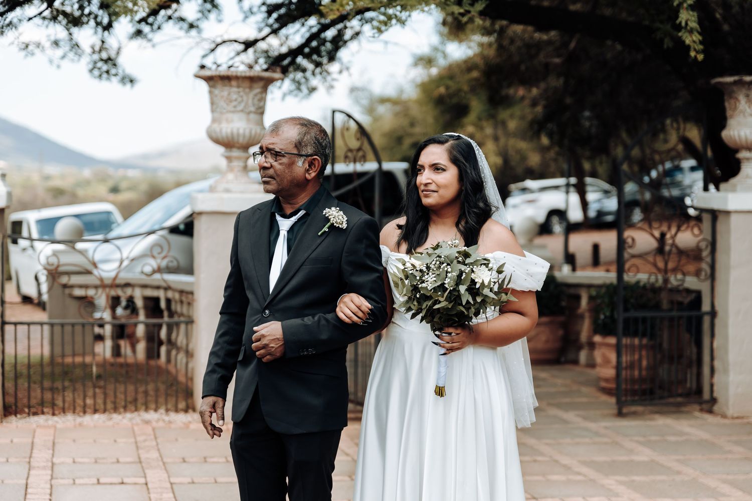 Wedding processional outdoors with stone pillars and mountain views in background.