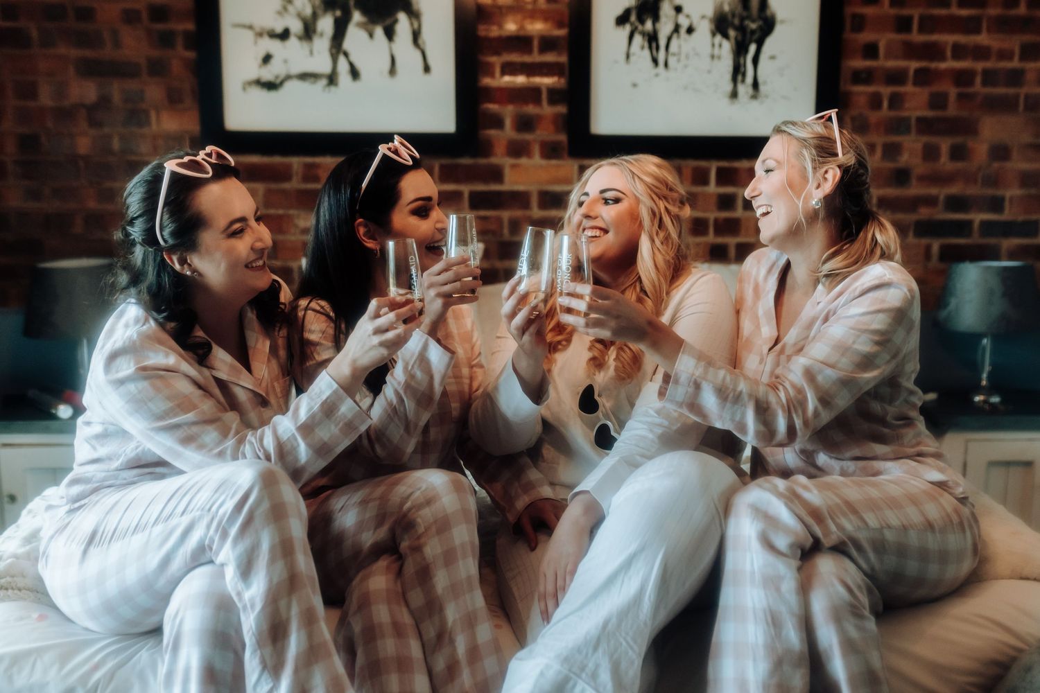 Friends in cozy pajamas laugh and celebrate together on a sofa with horse artwork in the background.
