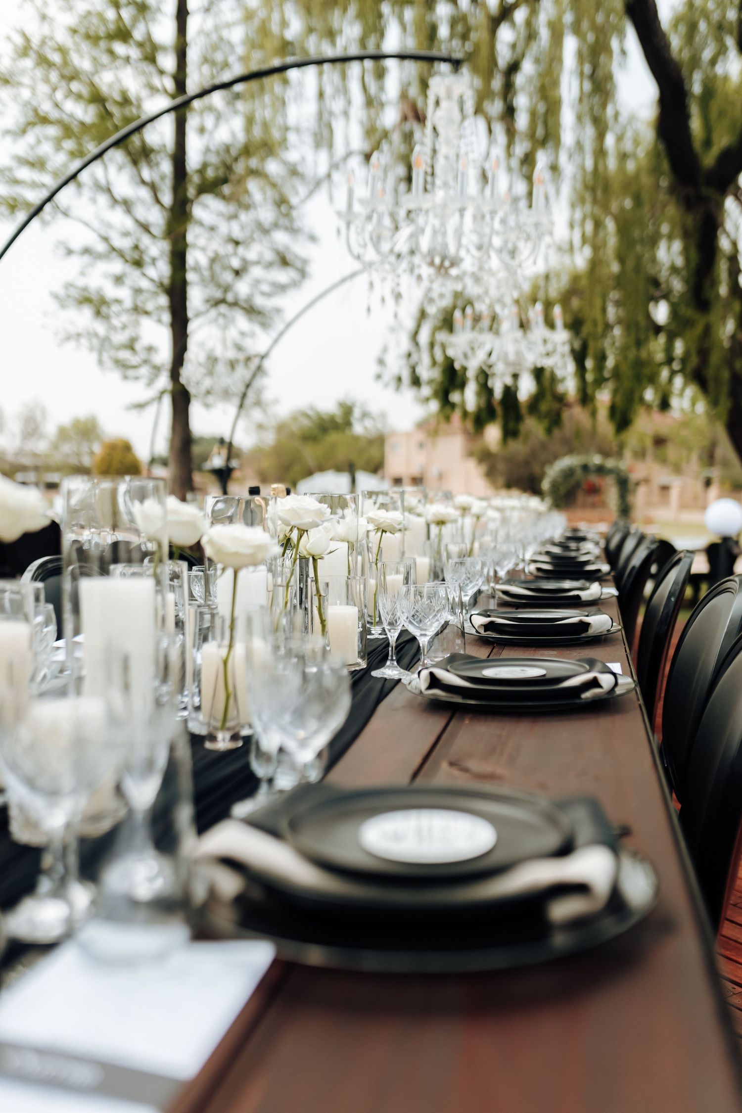 Elegant table setting with black charger plates, crystal glasses and white linens for an outdoor wedding reception.