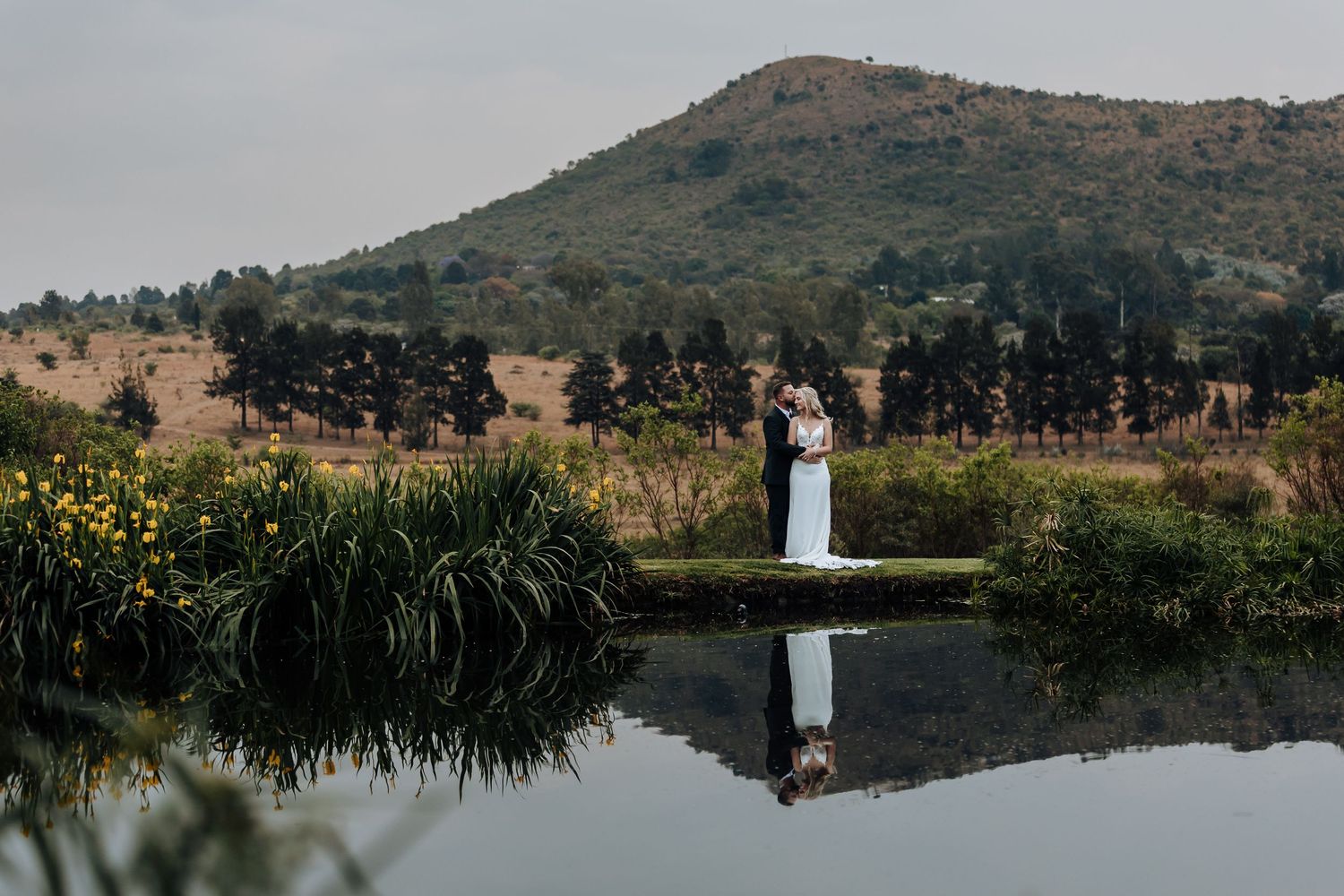 Scenic panoramic view of a lakeside wedding ceremony with mountain backdrop and natural landscape reflections in water.