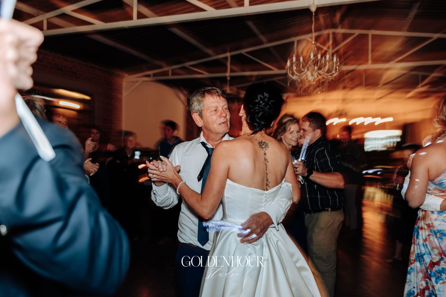 Bride and groom sharing first dance surrounded by guests at warmly lit wedding reception.