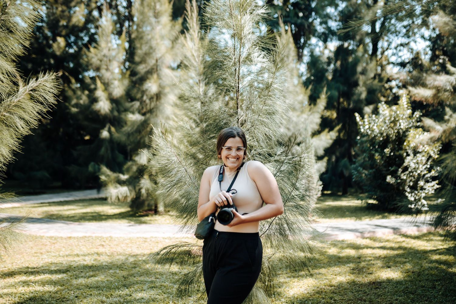 A photographer with camera stands among sunlit pampas grass in a garden setting.