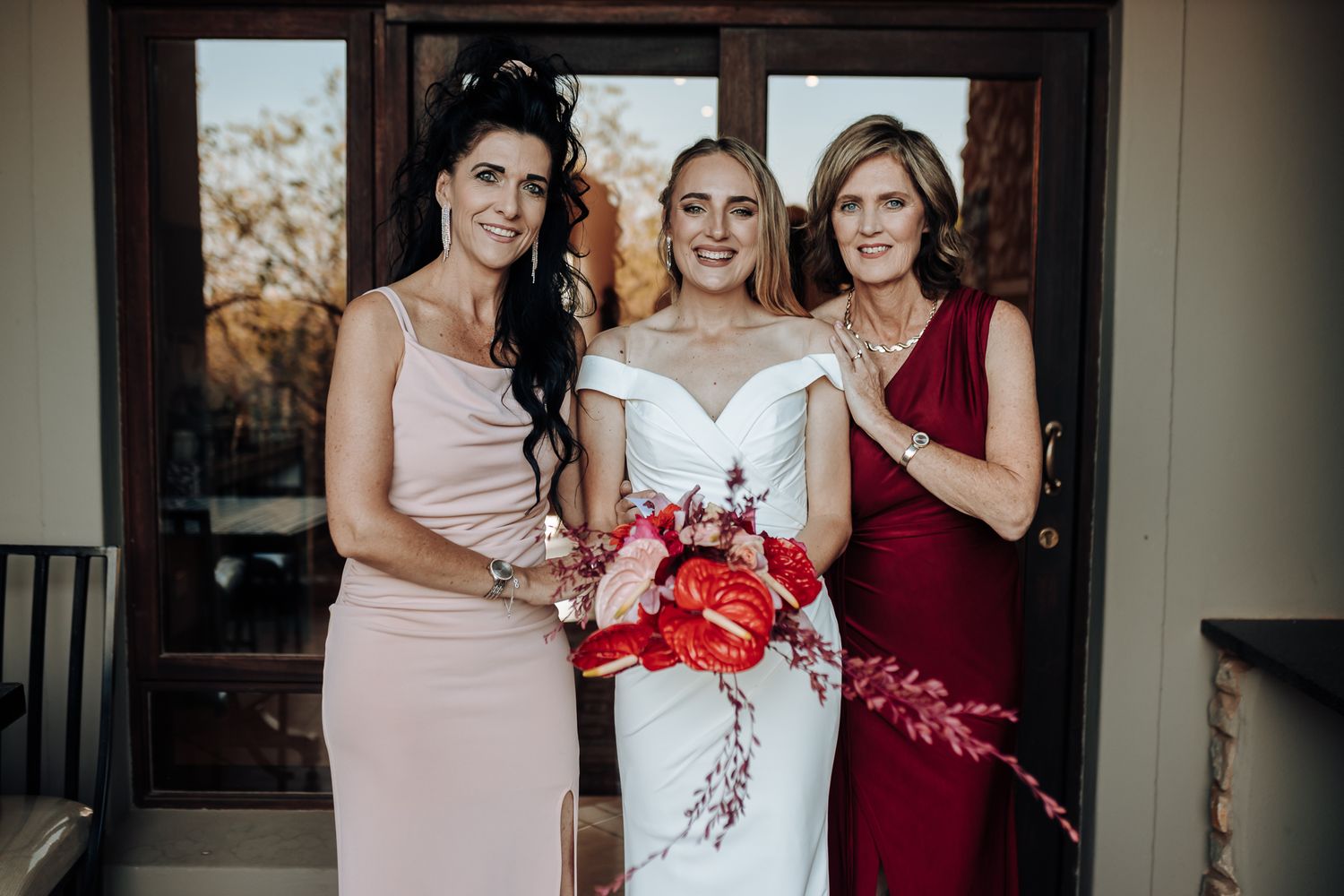 Wedding party poses together in coordinated pink and red formal dresses with floral bouquet.
