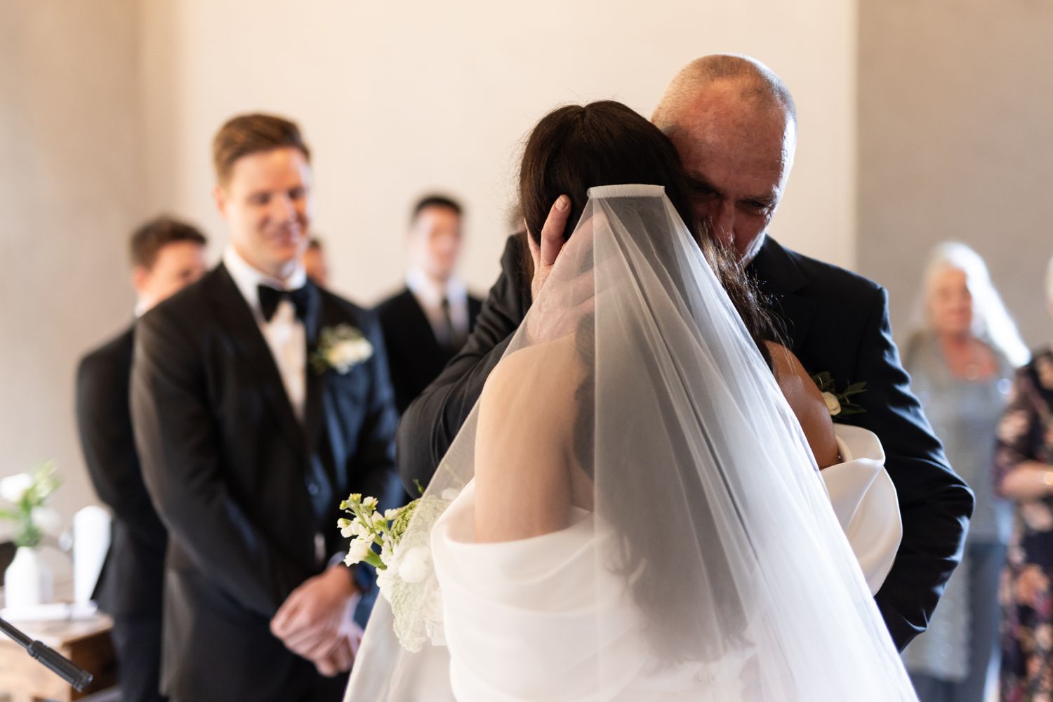 Intimate moment during wedding ceremony with guests watching in background.