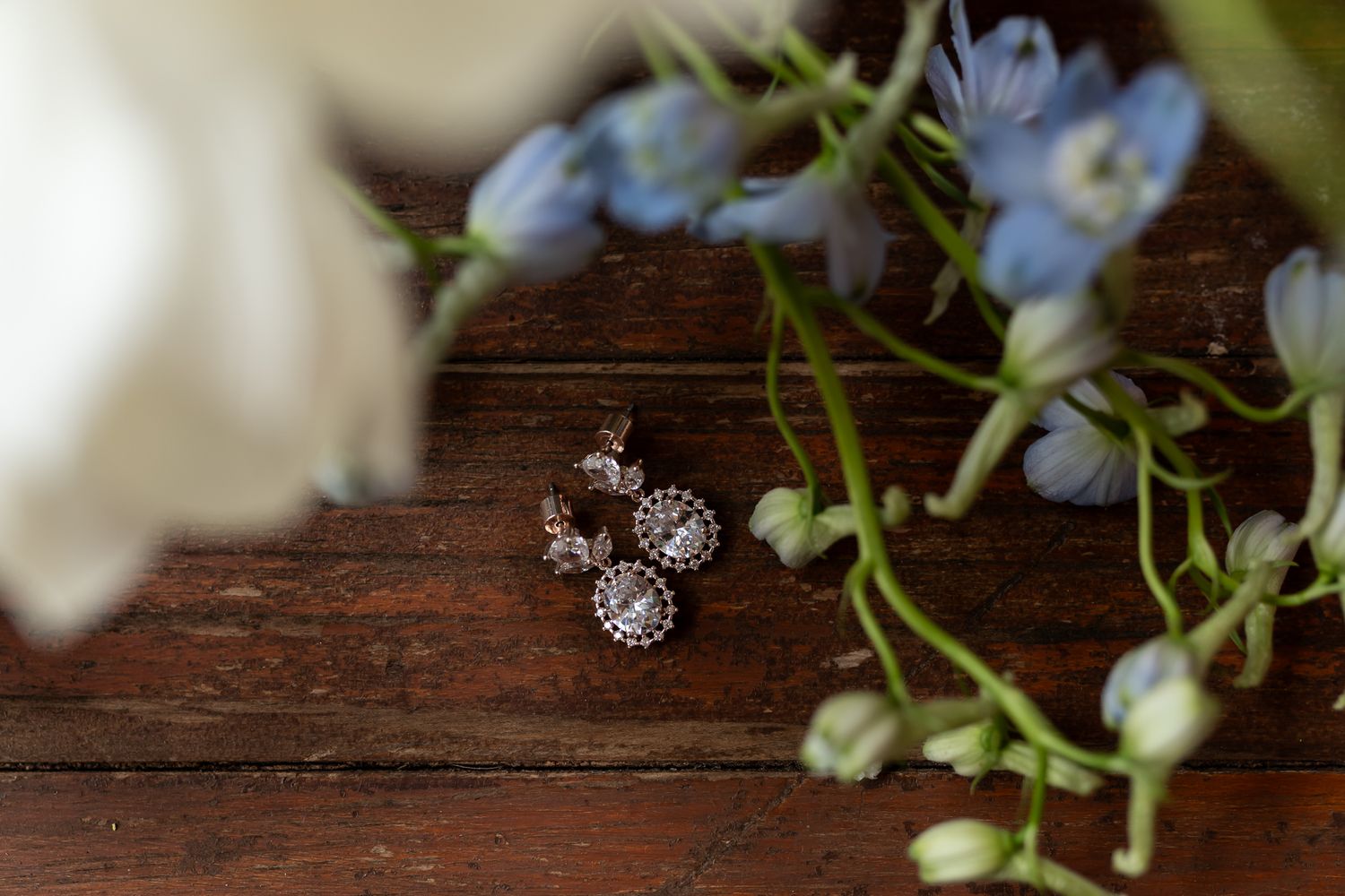 Close-up of sparkly wedding jewelry with delicate blue flowers on wood surface.